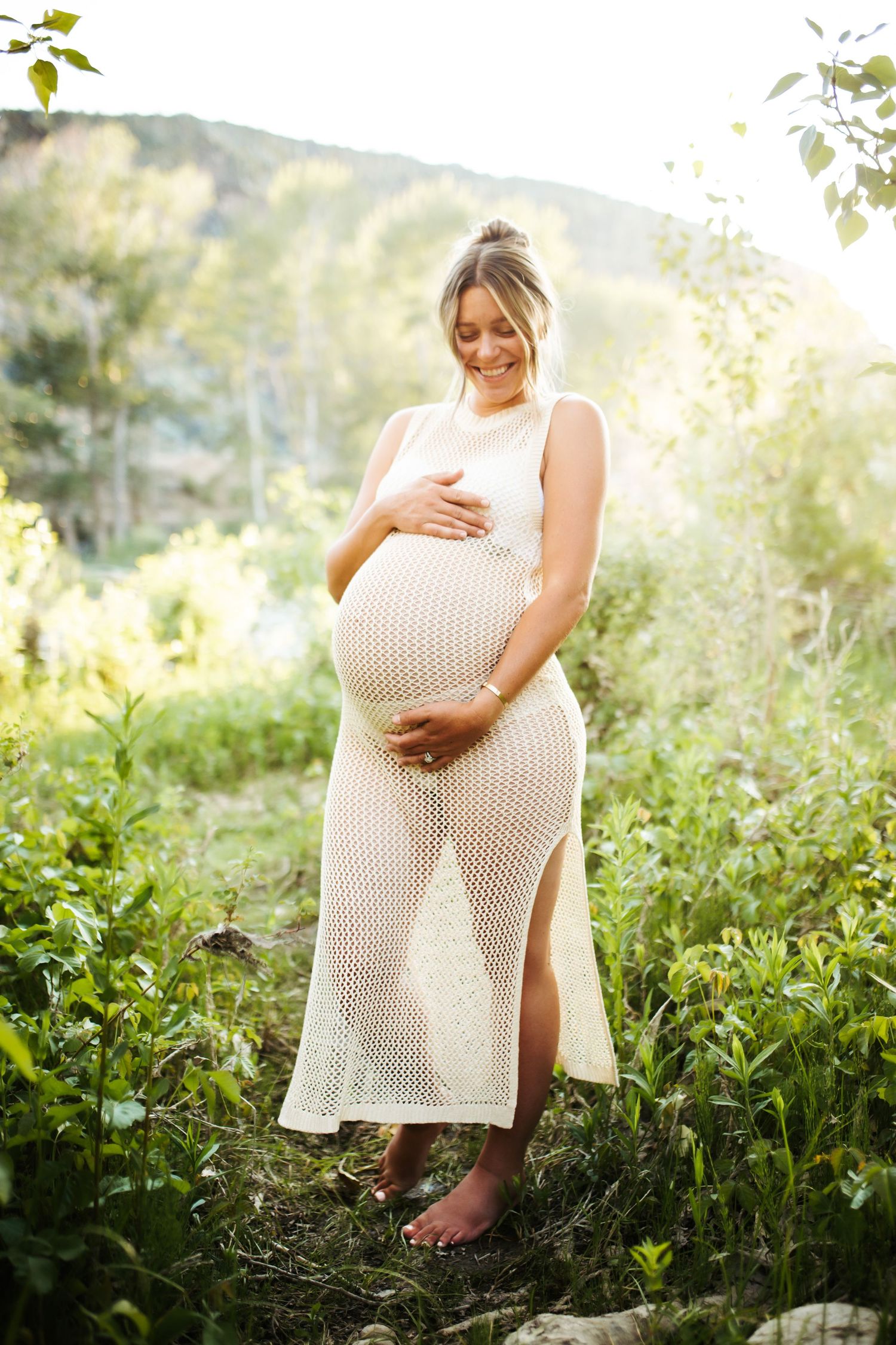 young woman holding her pregnant belly poses confidently for her maternity photos near Lucky Peak in Idaho