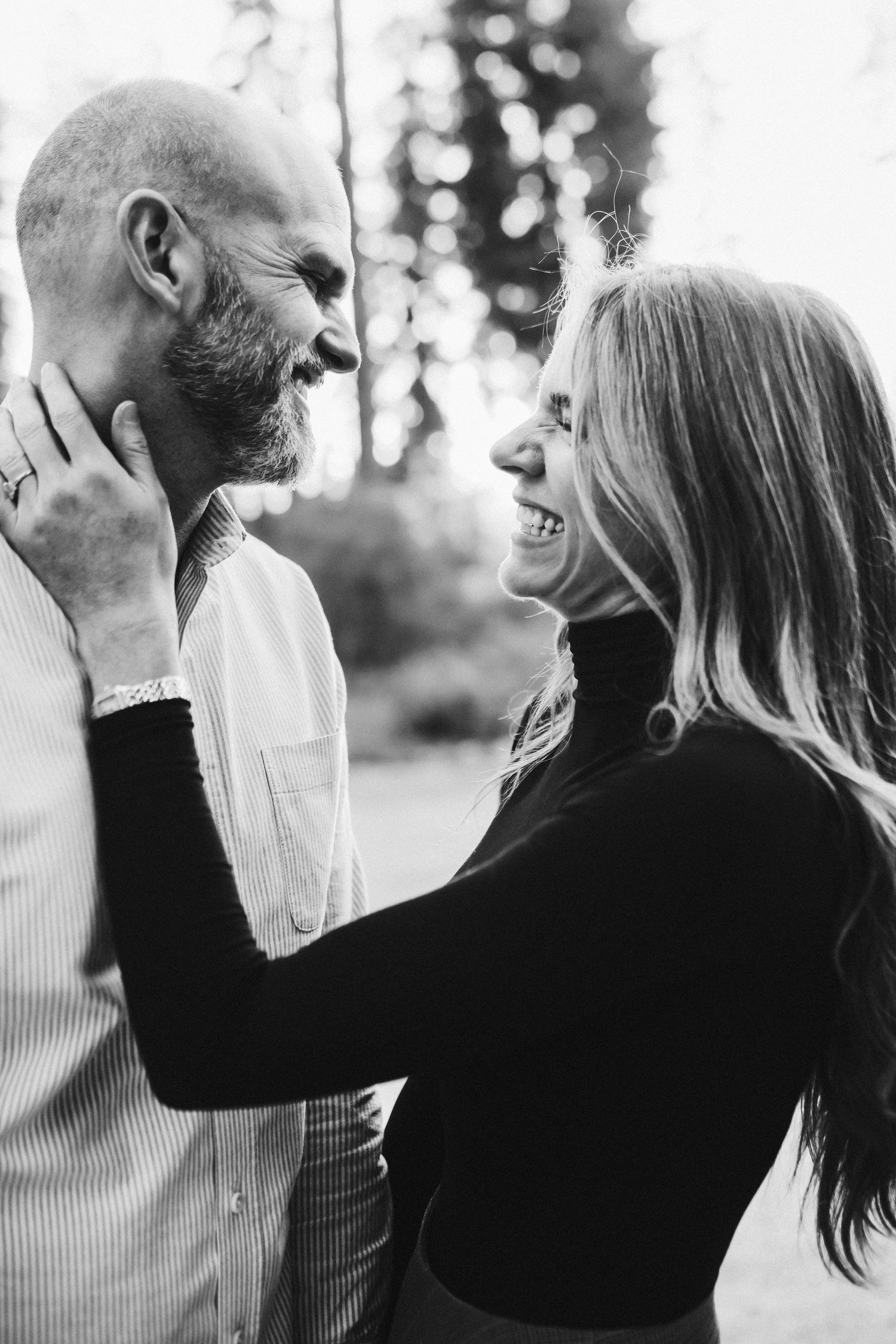 Black and white image of wife and husband laughing together during family photos in McCall