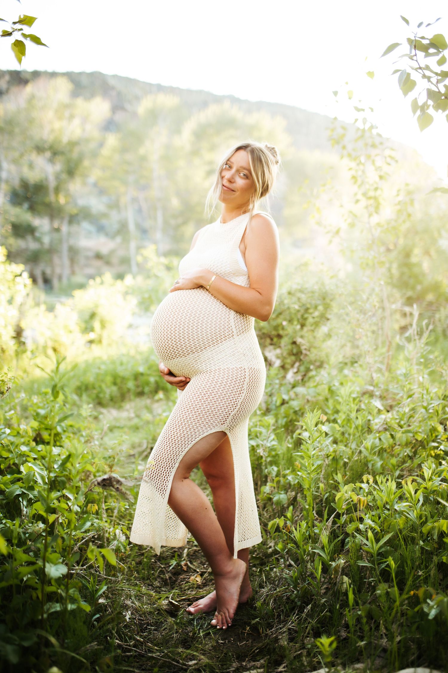 young woman holding her pregnant belly poses confidently for her maternity photos near Lucky Peak in Idaho
