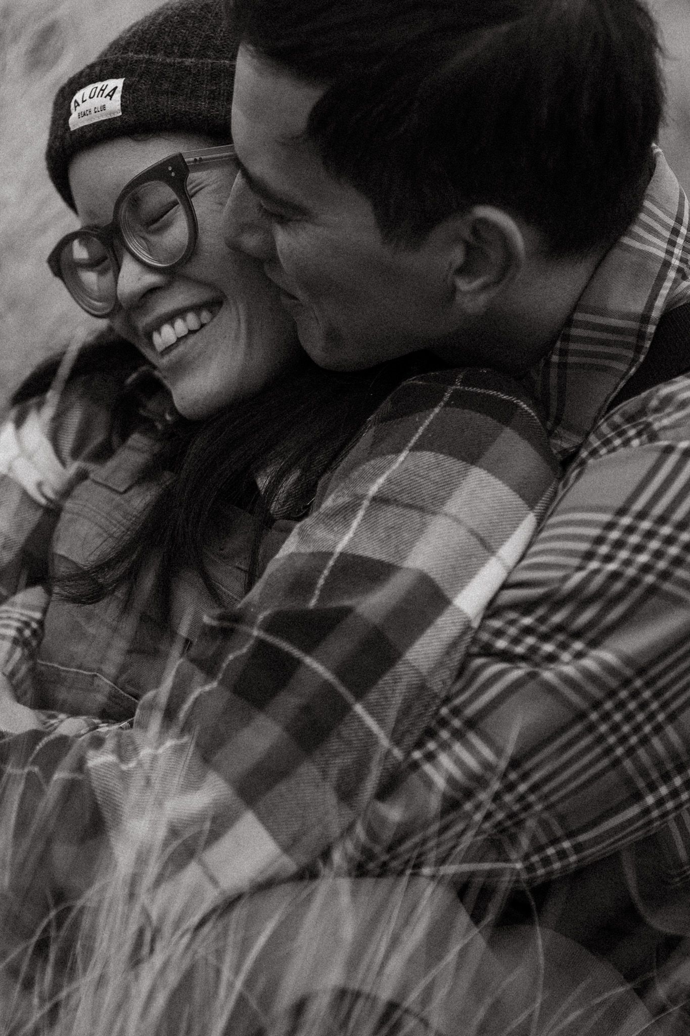 Black and white image of husband kissing his wife on the cheek for a photoshoot