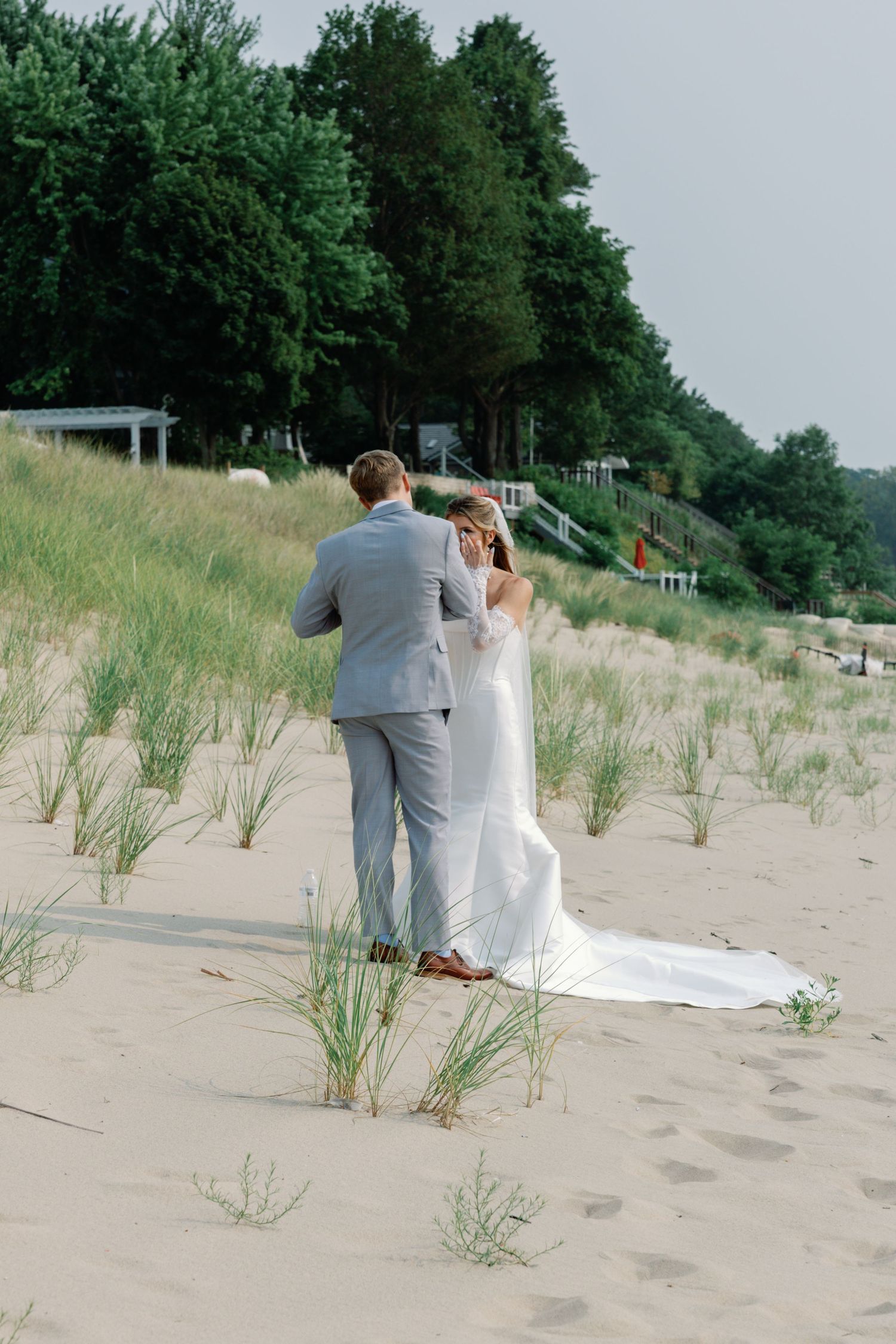 Wedding couple walks through beach grass and sand dunes during their photoshoot.
