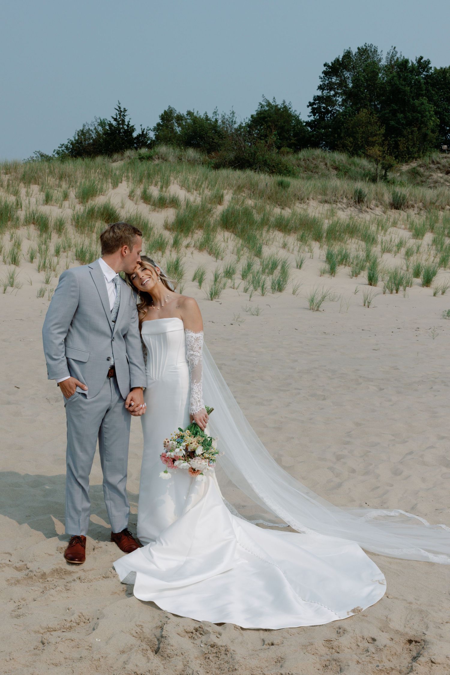 A romantic beach wedding photoshoot with a couple posing on sandy dunes at sunset.