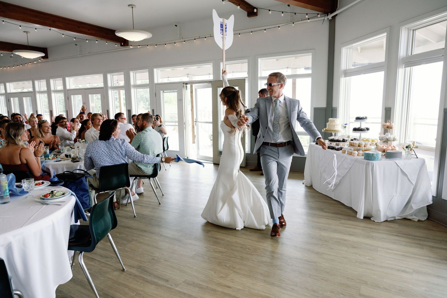 Wedding reception venue with white tablecloths and large windows overlooking water.