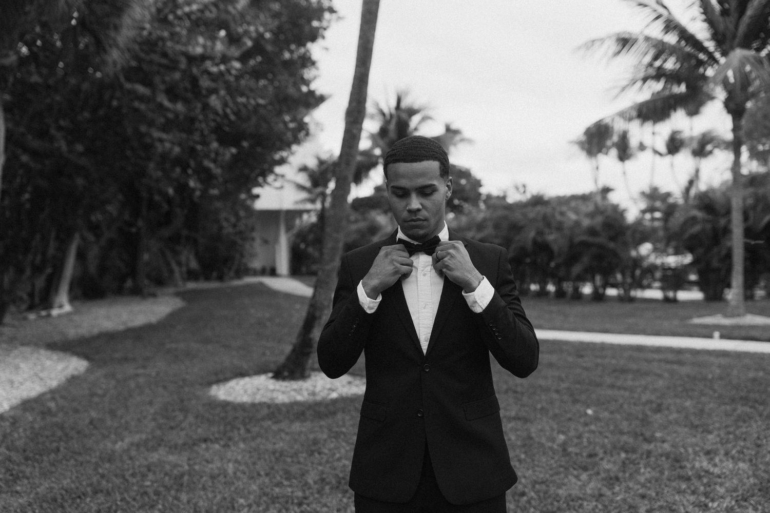 A series of photos showing someone adjusting their formal black suit and tie outdoors.