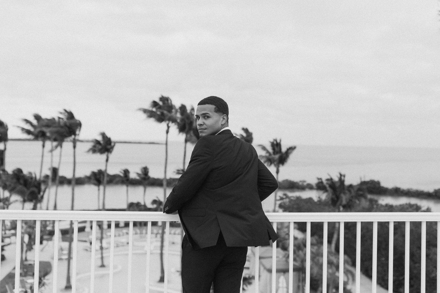 Wedding couple poses on a balcony overlooking a scenic tropical beach resort.