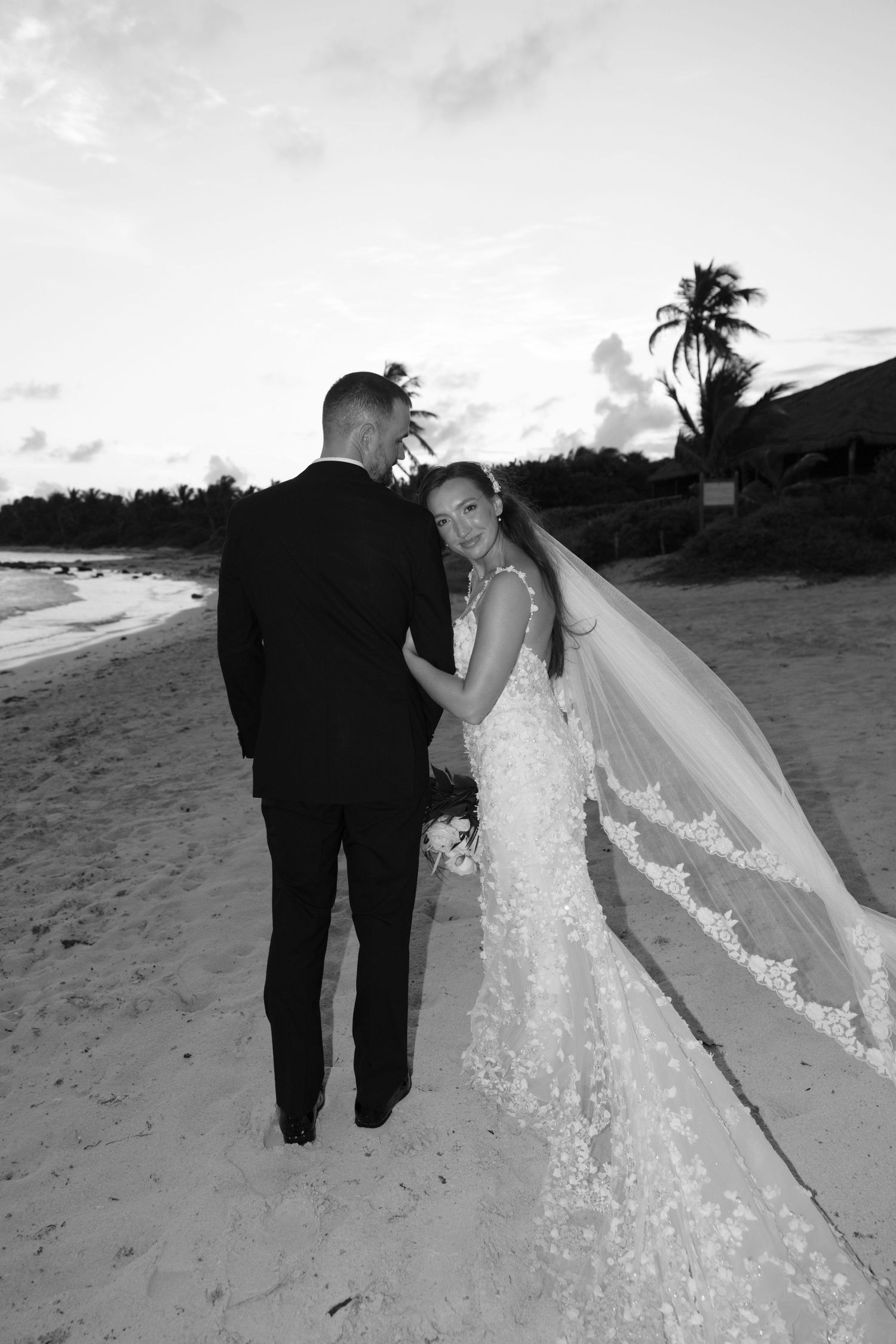 Artistic black and white beach wedding photos showing a long lace veil flowing in the wind.
