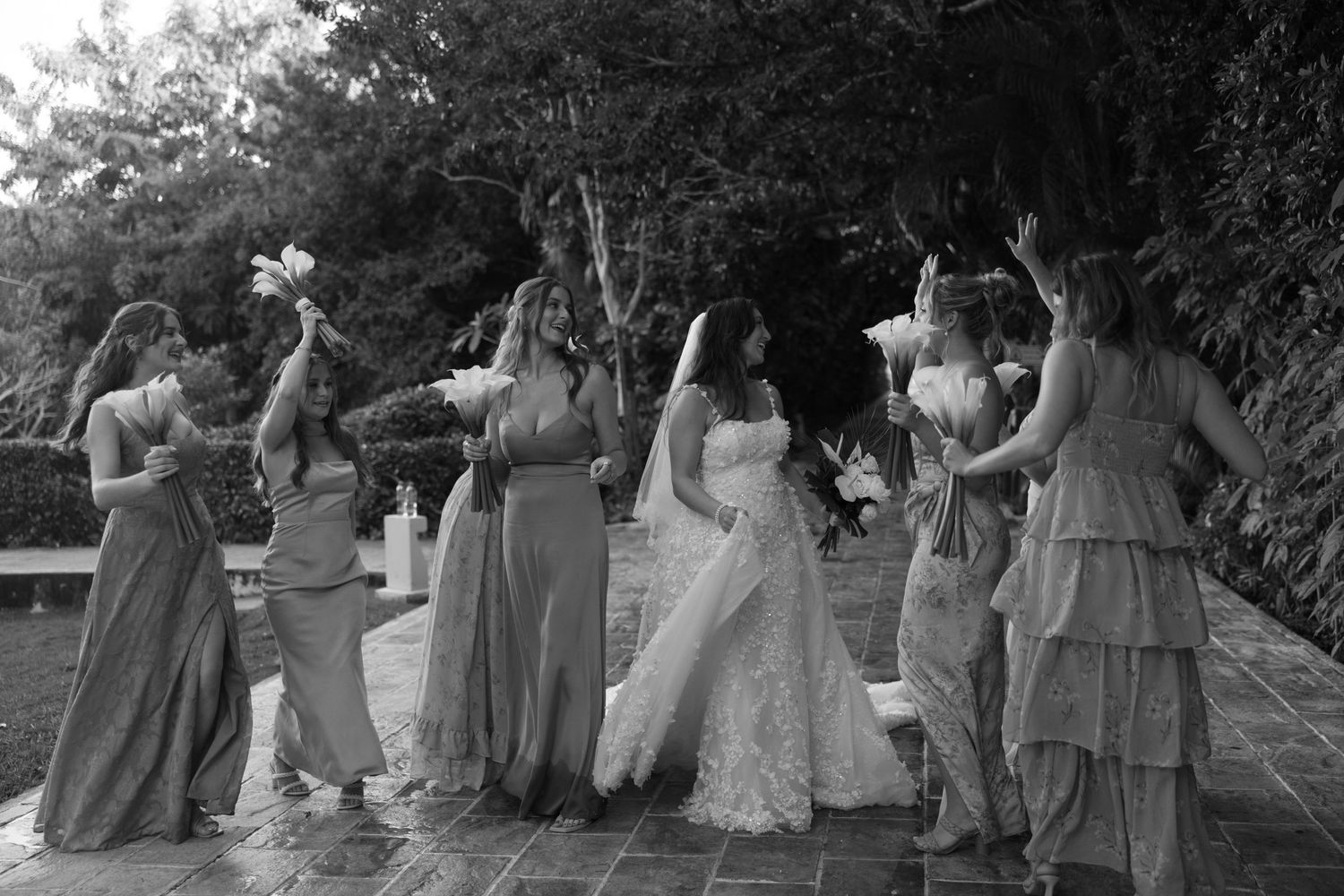 Black and white photo of wedding party members in formal attire outdoors.