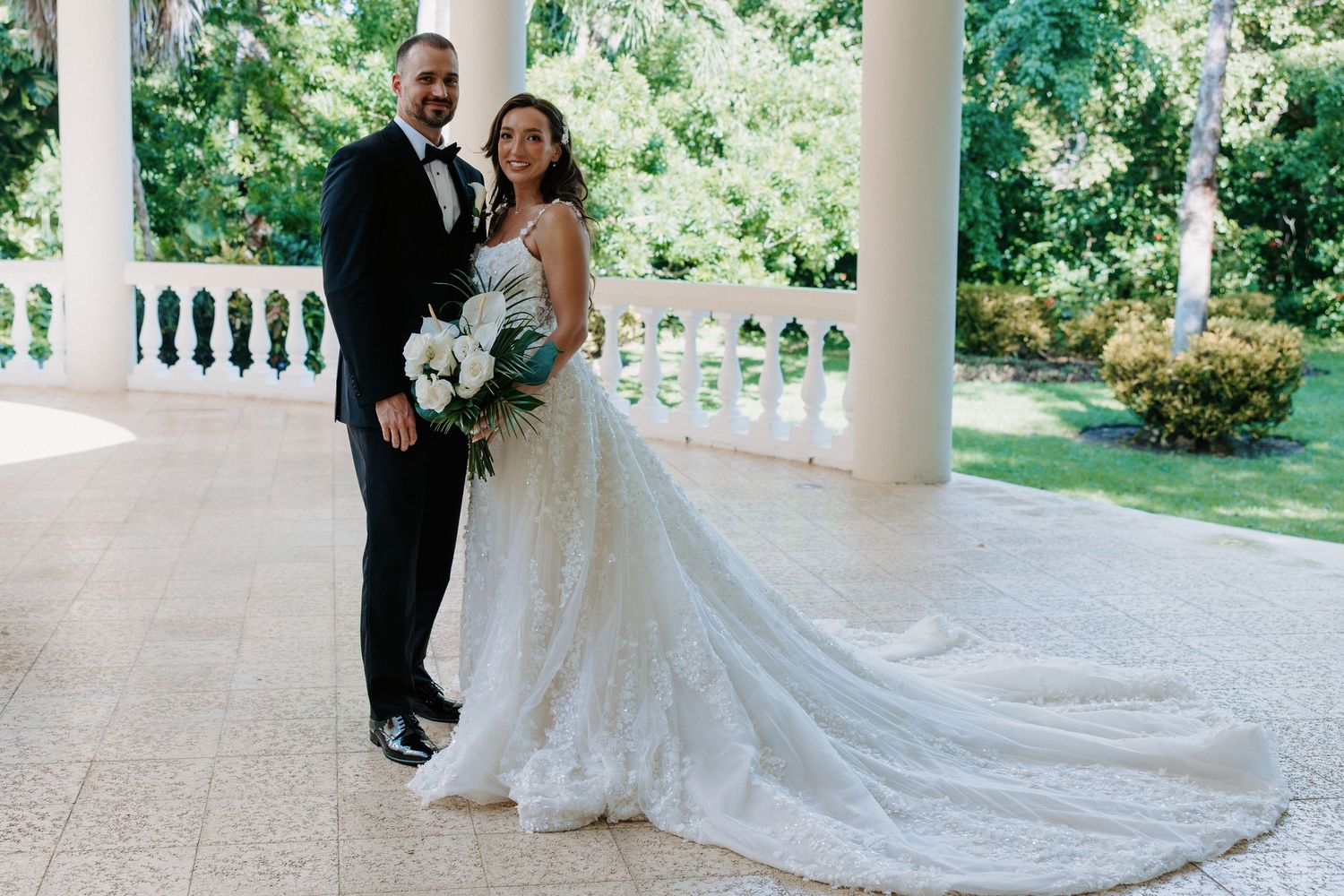 Elegant wedding party gathering under white columned porch with flowing bridal gown.