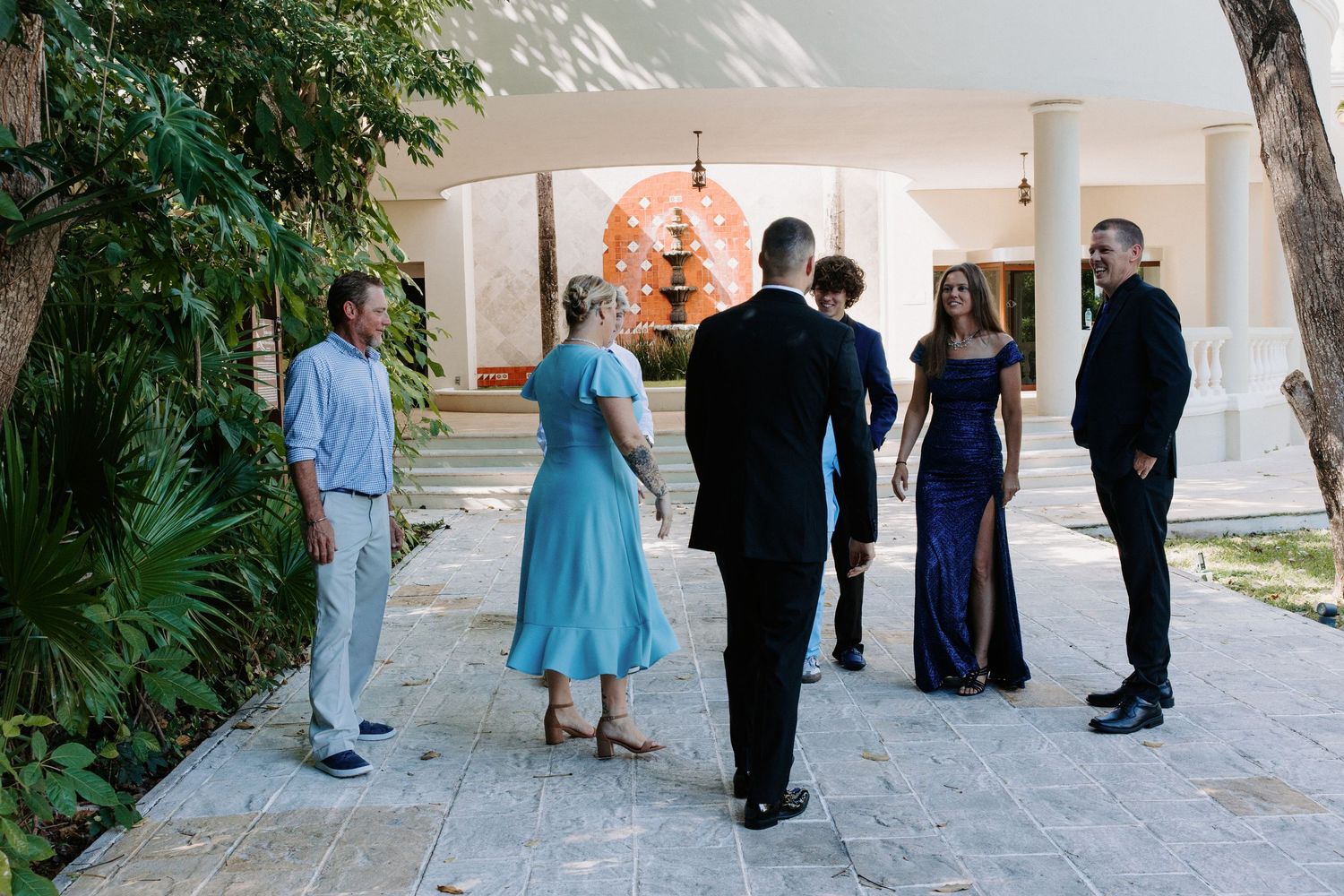 Wedding party gathers on an elegant outdoor terrace with tropical landscaping.