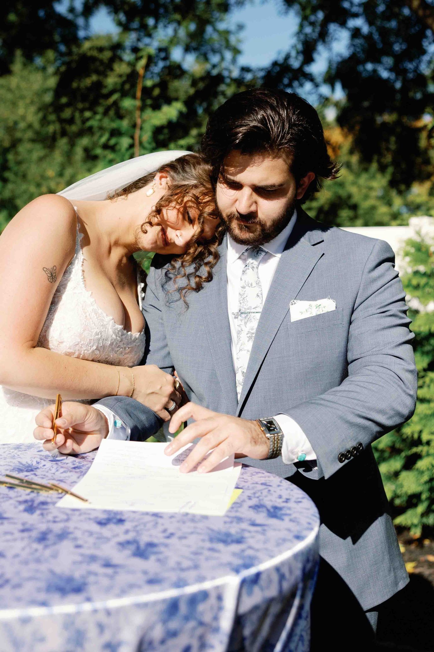 A couple signs marriage documents together at an outdoor wedding ceremony.