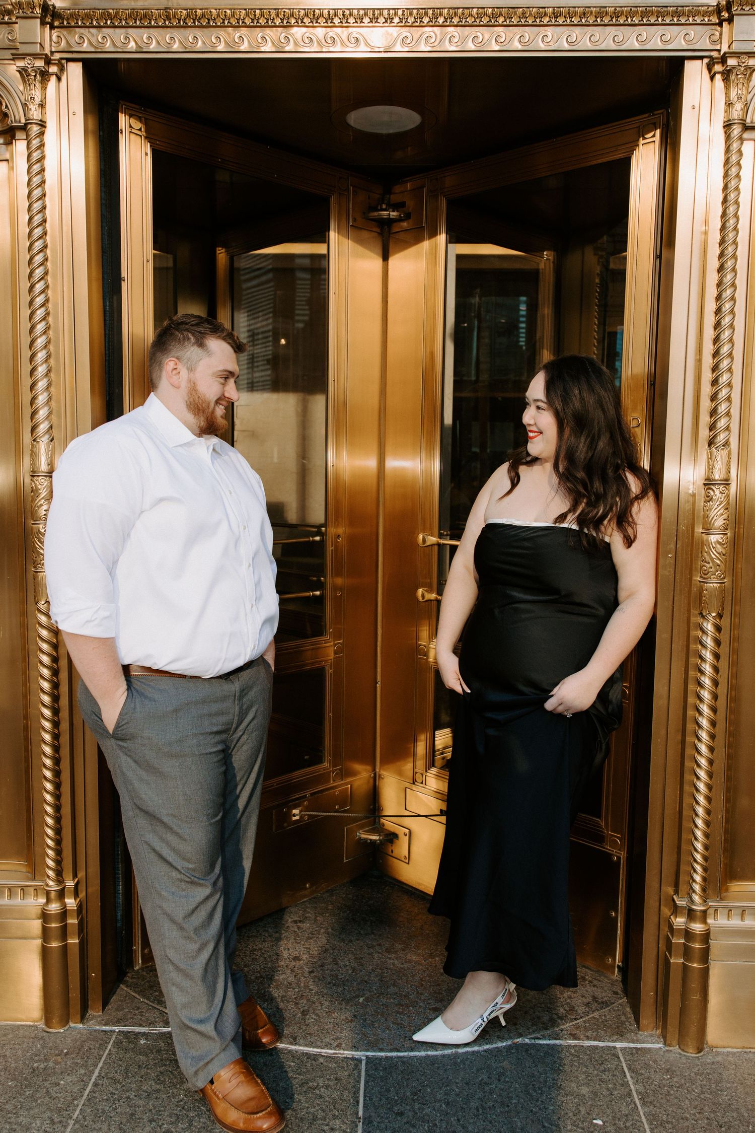 A couple in formal wear shares an intimate moment in an ornate hallway with gold-trimmed details.