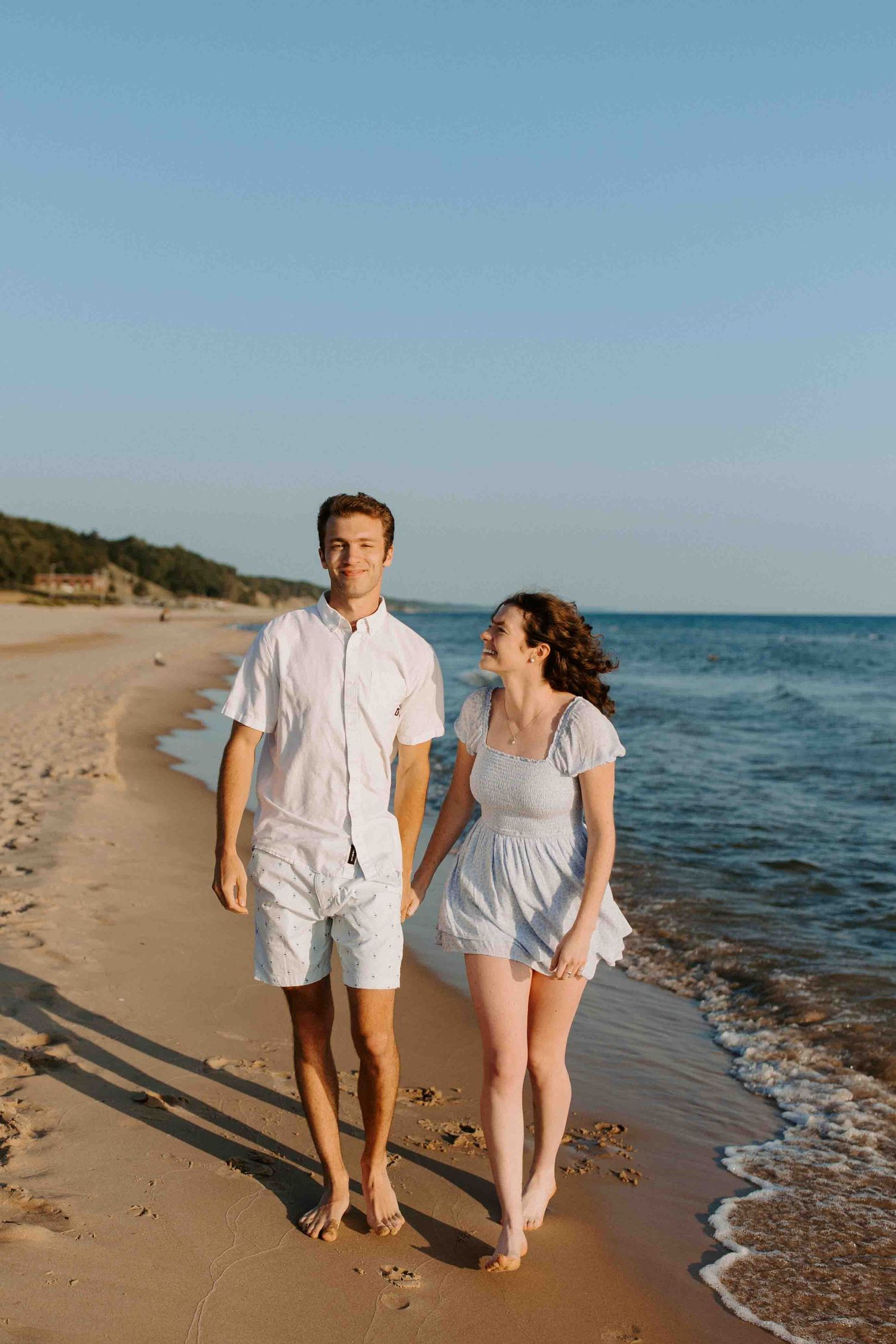 Couple walking together on sandy beach at sunset by the ocean.
