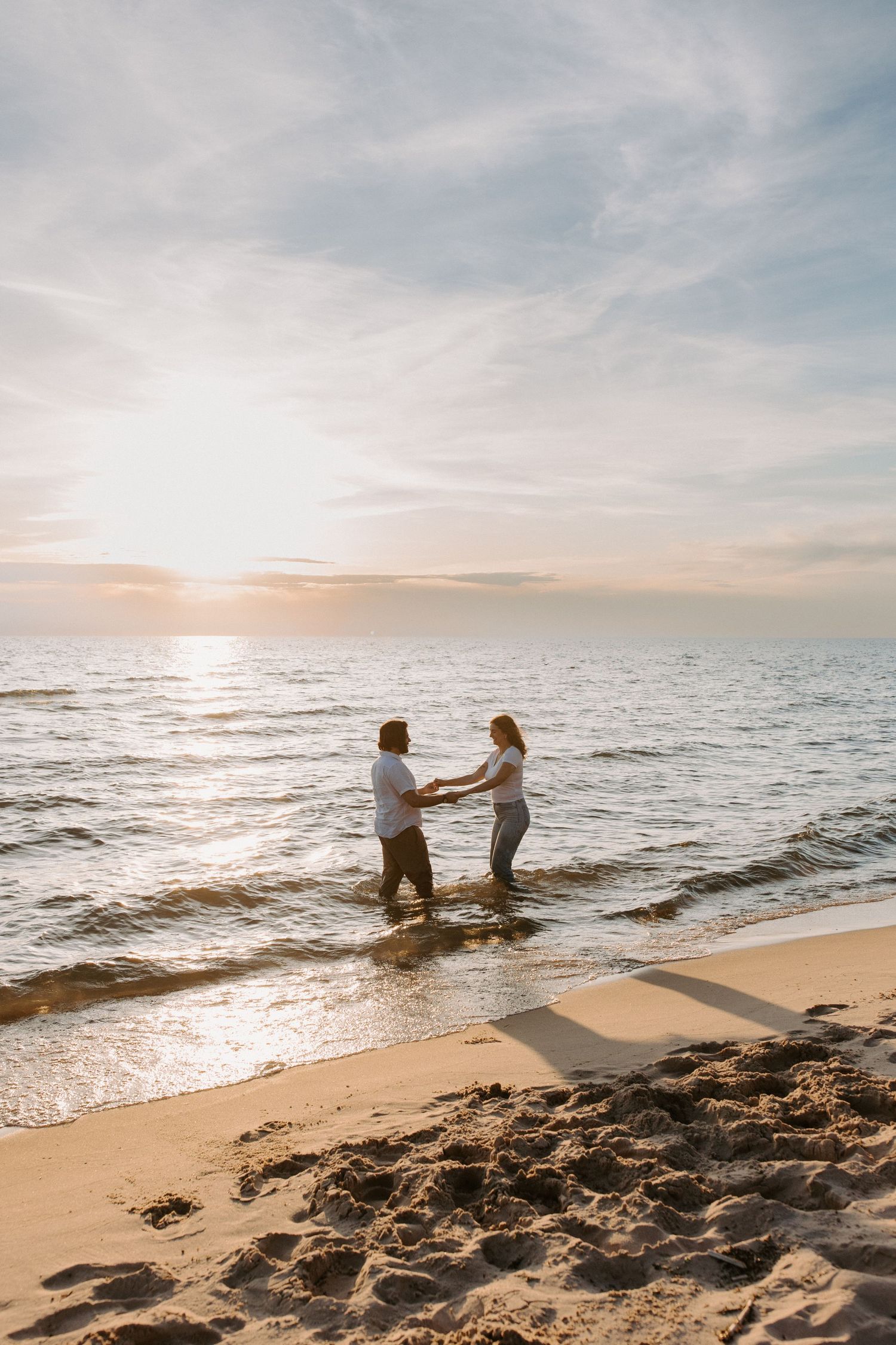 Couple playing in the ocean waves at sunset on a sandy beach.