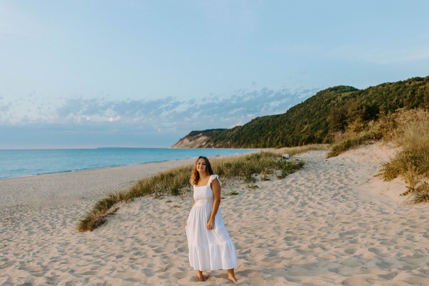 A flowing white dress contrasts against sandy dunes and ocean views.