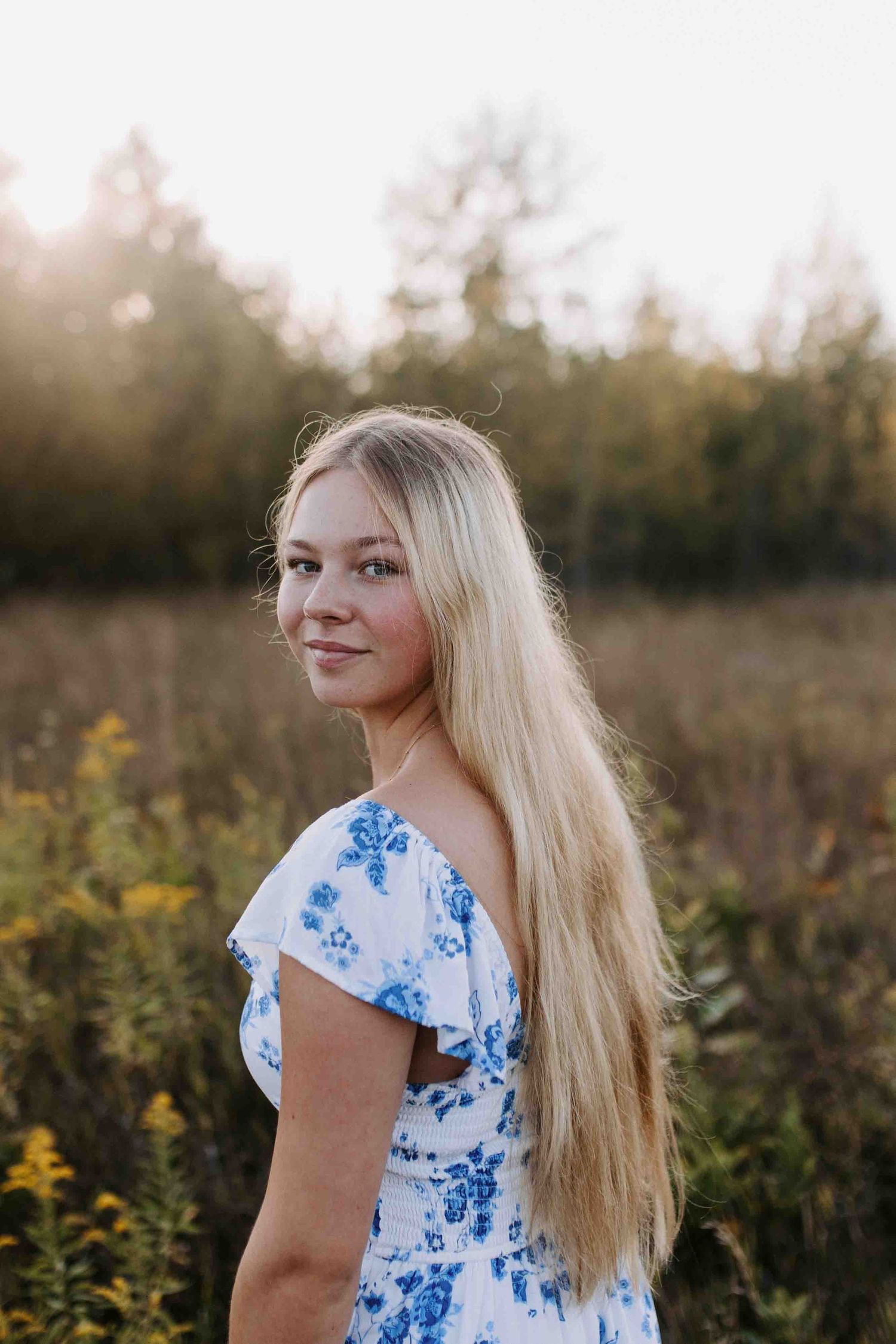 Person in blue floral dress poses in golden field during sunset.