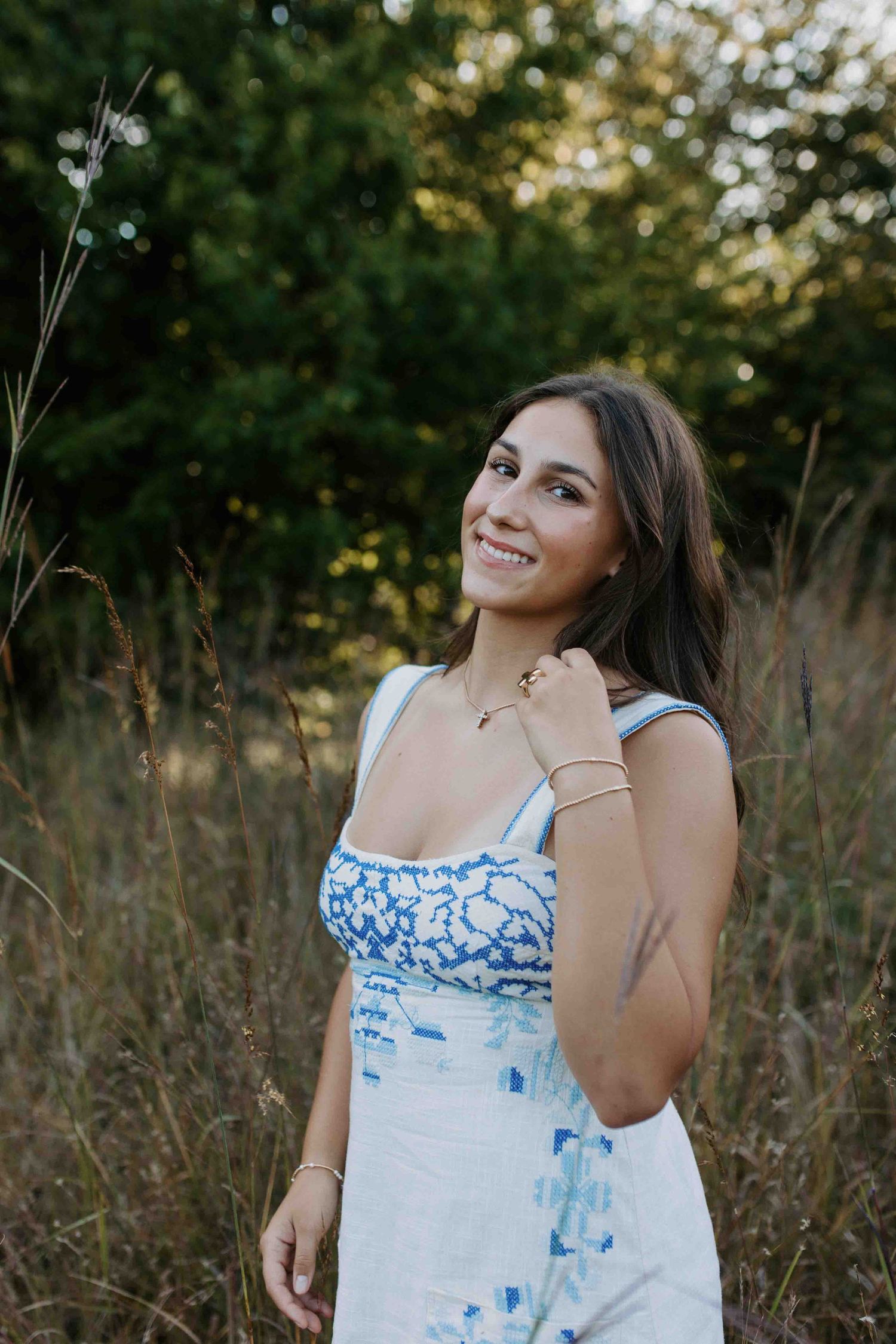 Summer portrait in a white dress with blue details against natural foliage backdrop.