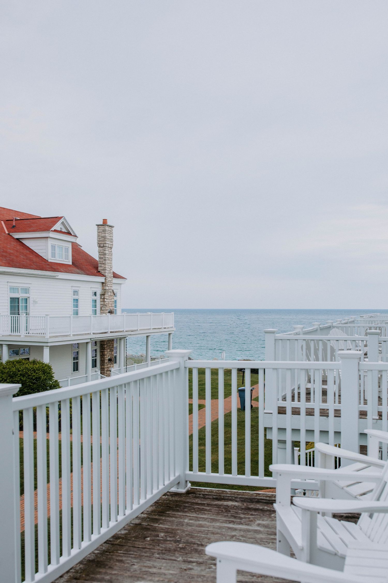 Ocean view from a white-railed deck of a coastal vacation home with blue waters in the distance.