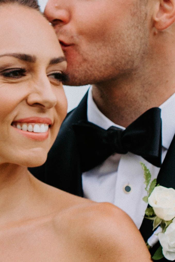 Close-up wedding portrait showing tender affection between bride and groom with white floral boutonniere.