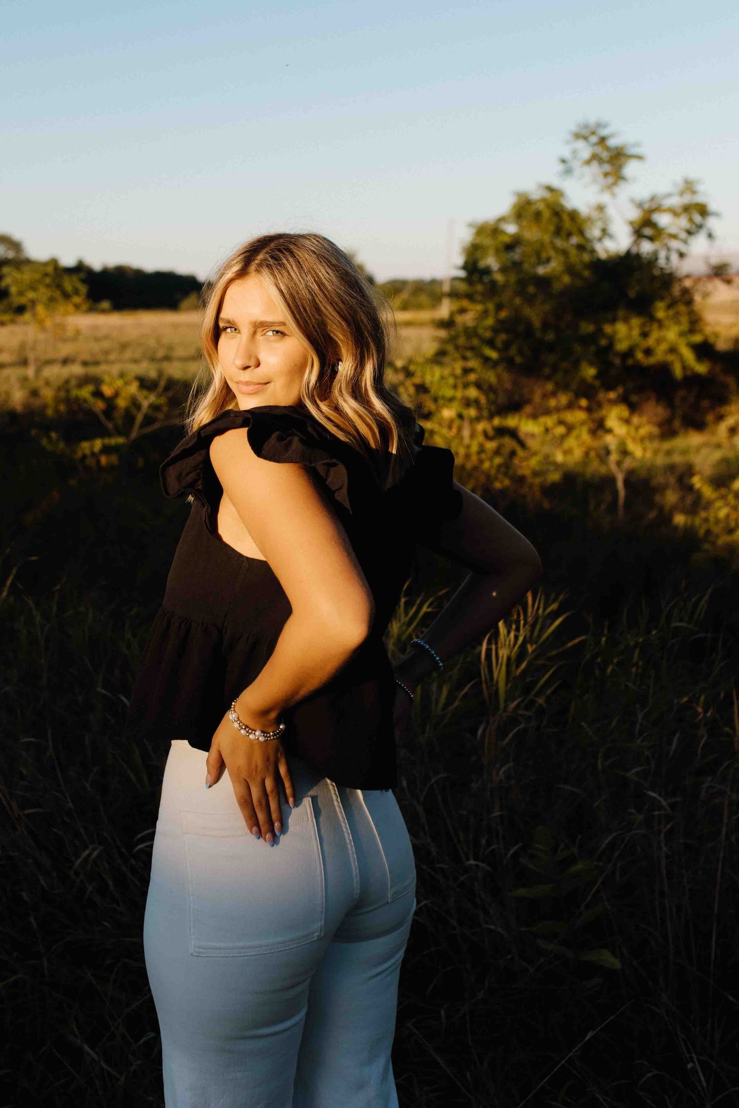 A golden hour outdoor portrait featuring someone in a white and black outfit against a rural landscape.