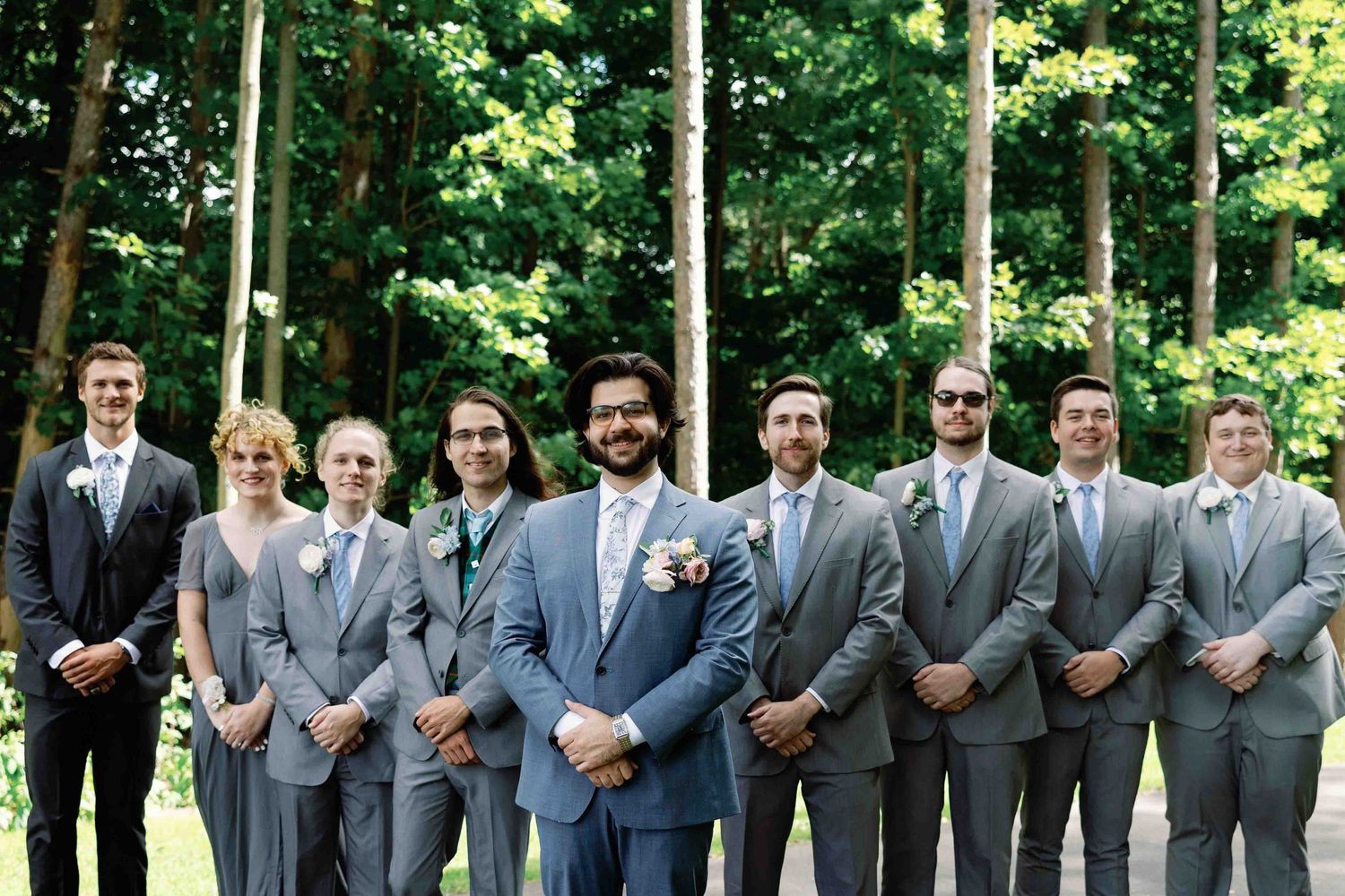 Wedding party members in coordinated gray suits pose together outdoors.