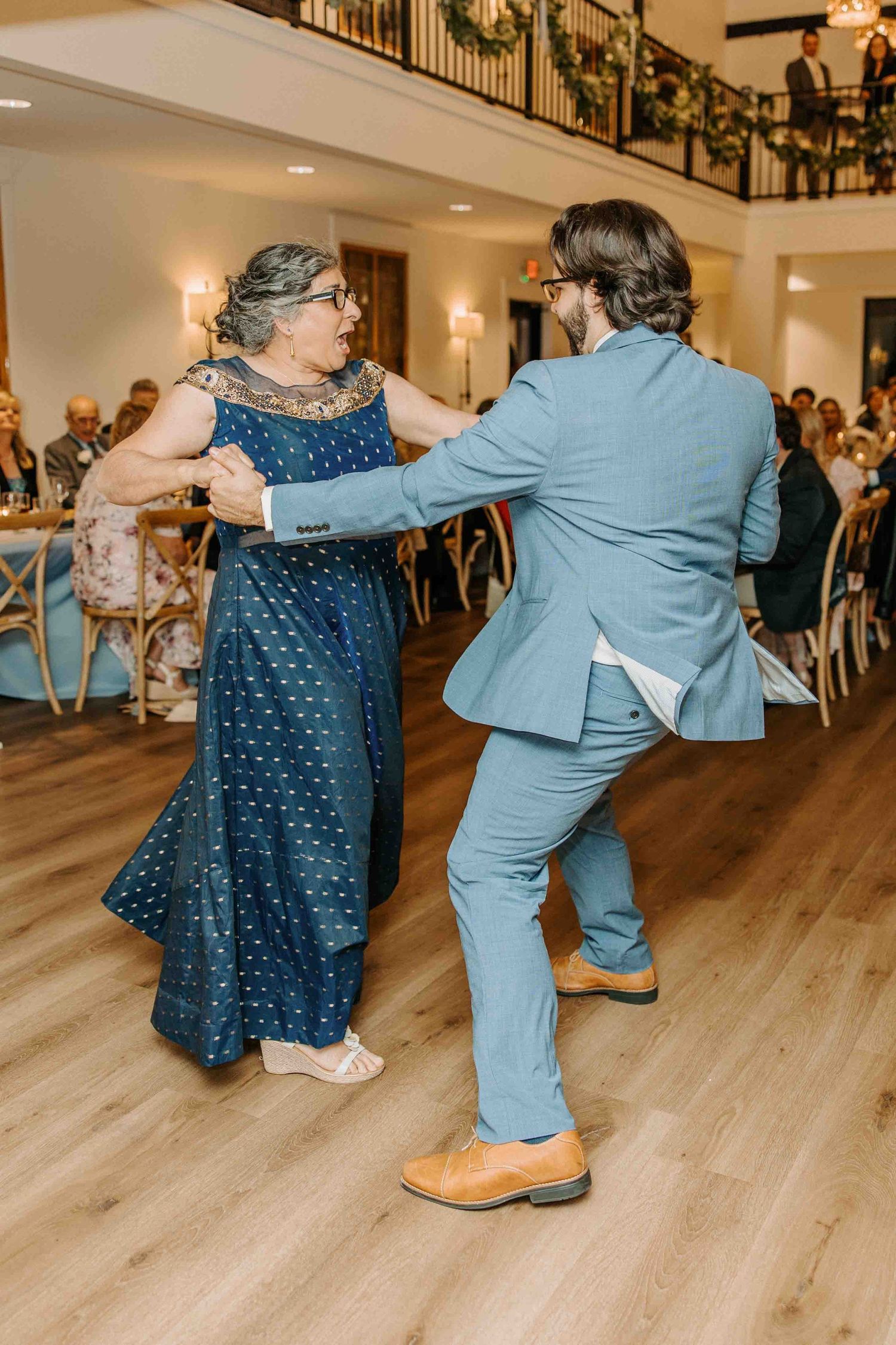 Wedding guests perform choreographed dance moves on a light wooden floor.