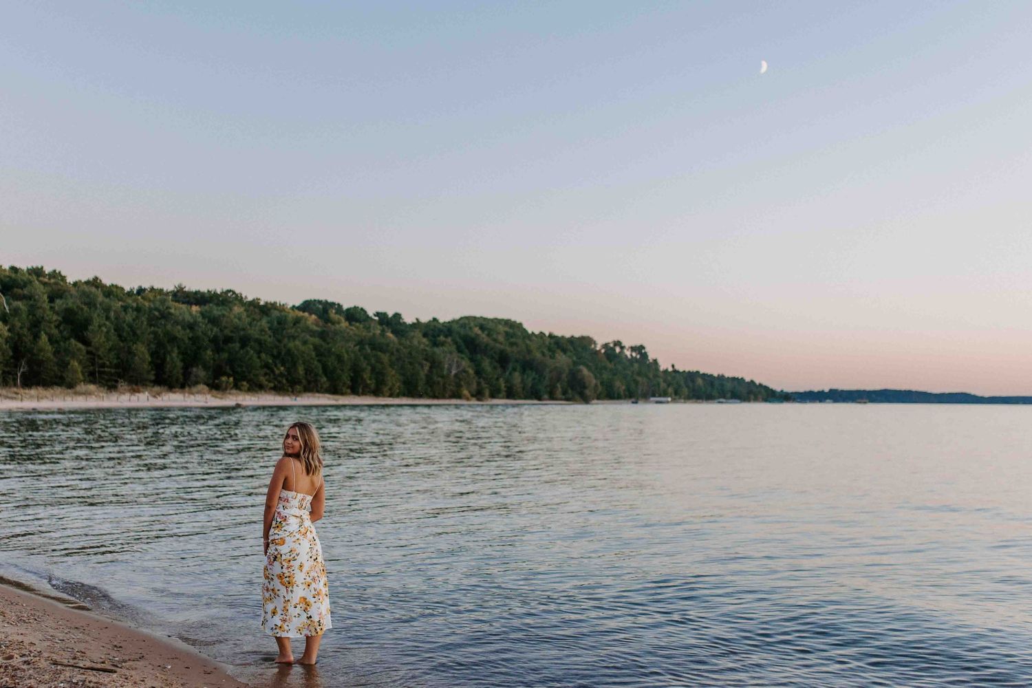 Panoramic view of a lakeside beach during golden hour with trees lining the shore.