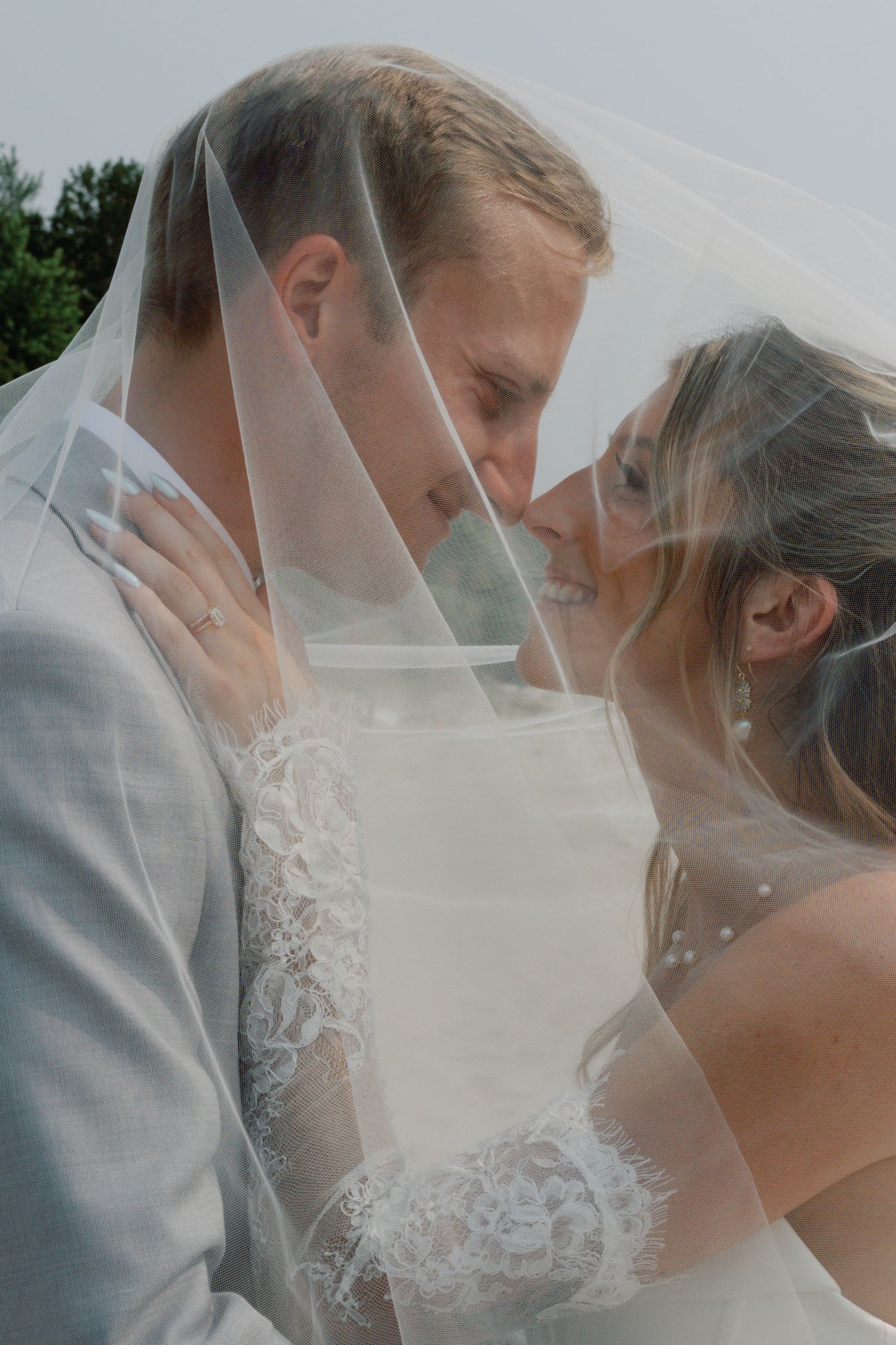 Romantic beach wedding couple sharing an intimate moment under a delicate white veil.