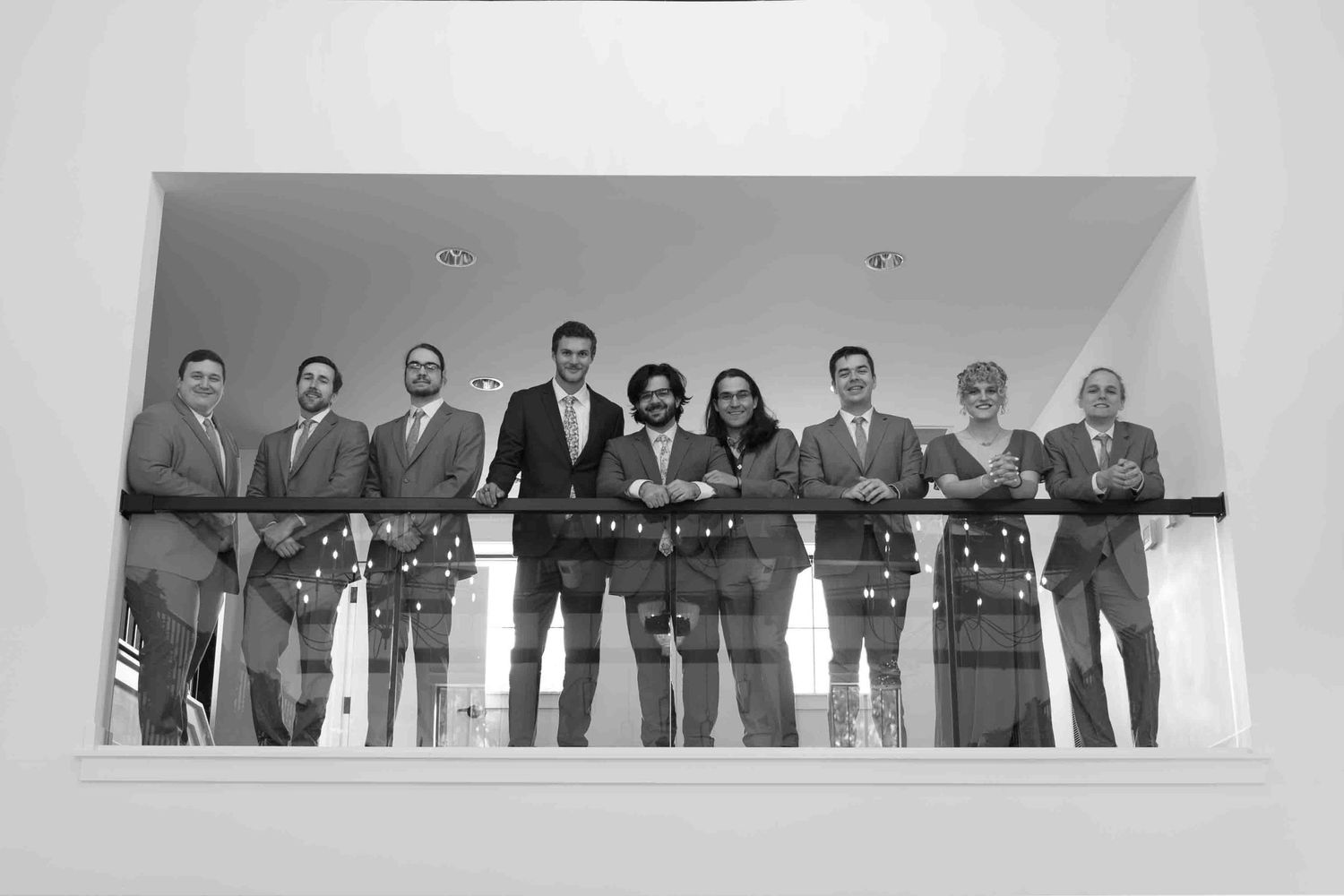 A group of people standing together in business attire in front of a light colored wall.