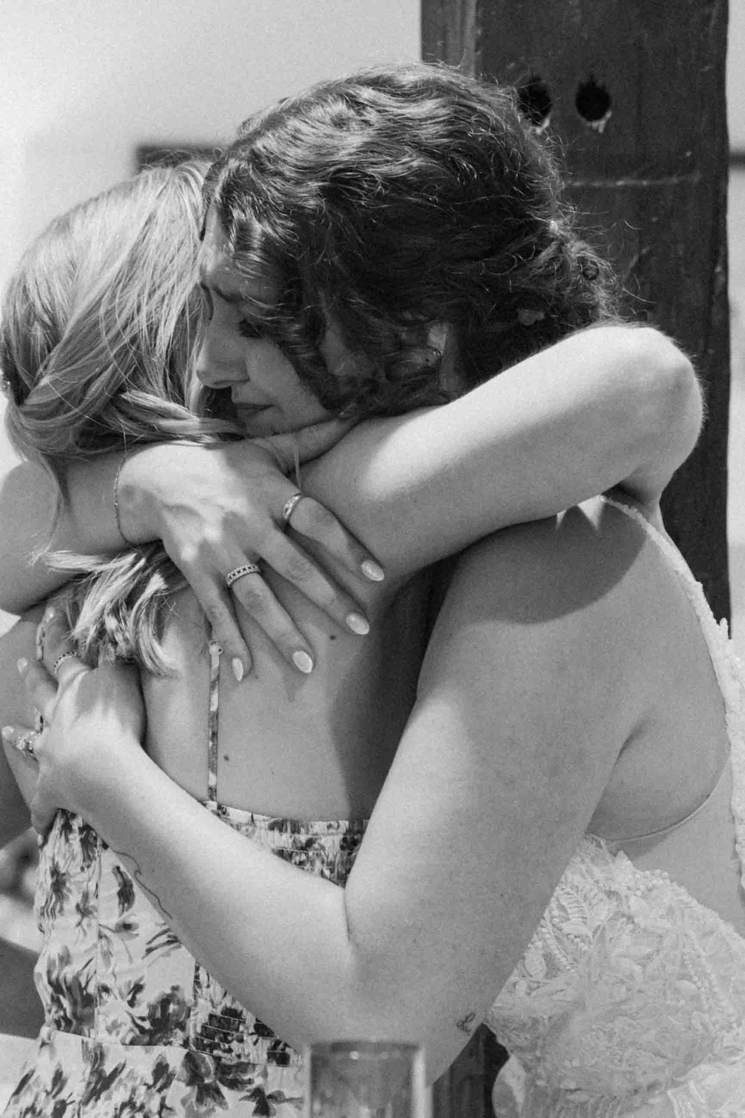 Emotional embrace between wedding attendees wearing floral dresses.