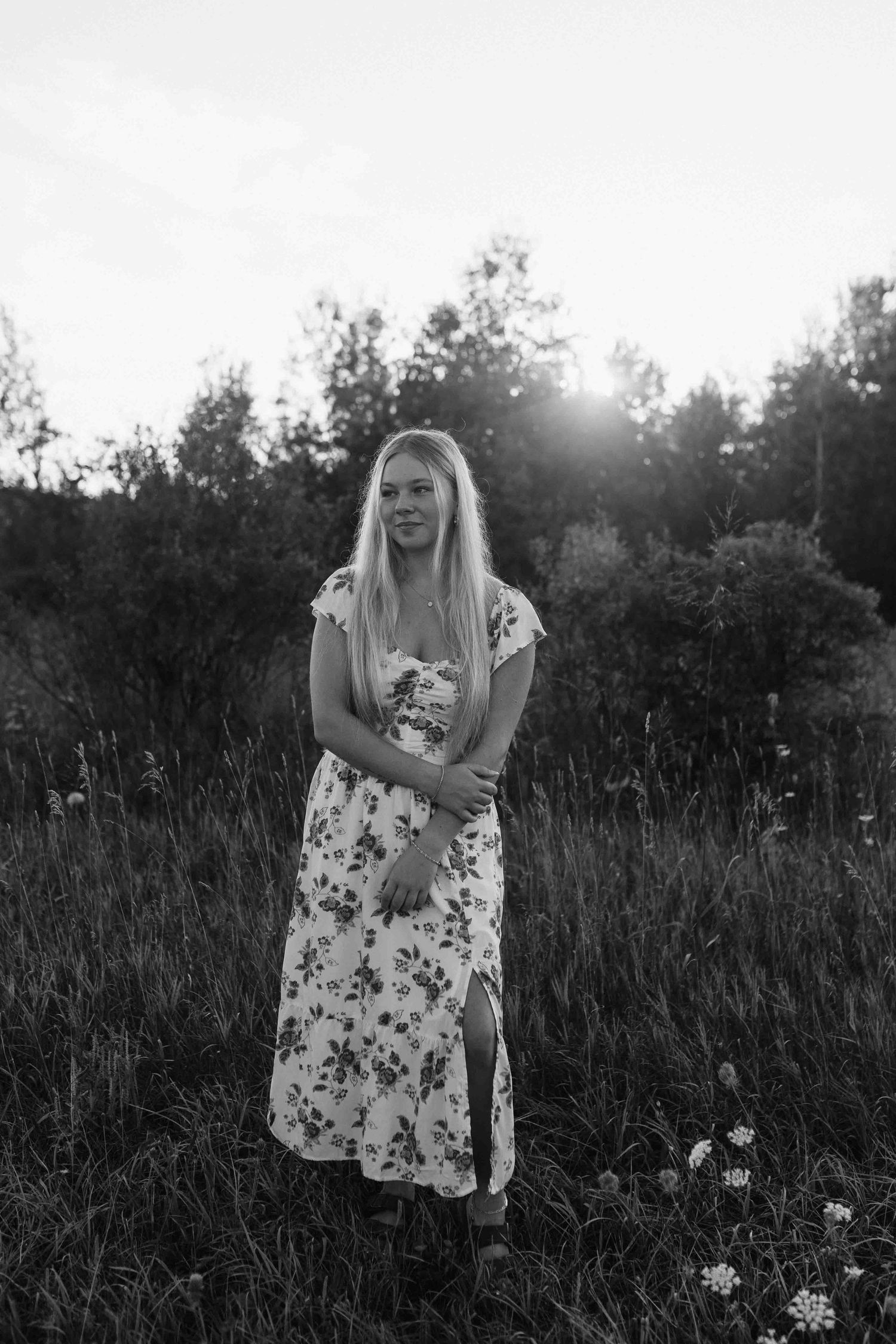 Black and white portrait in a meadow showing a floral dress against tall grass and trees.