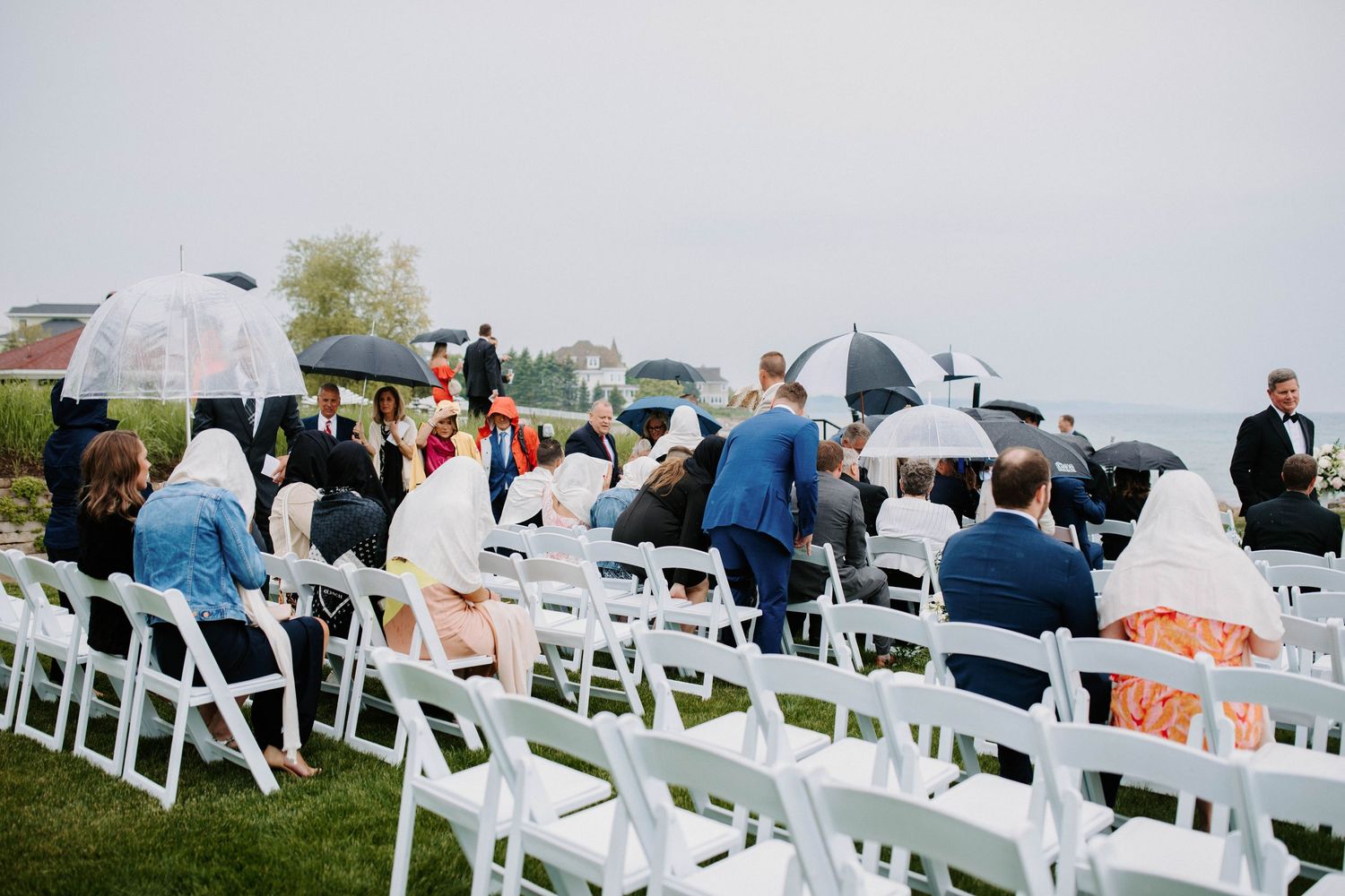 Wedding ceremony seating with white chairs arranged on grass overlooking the water.