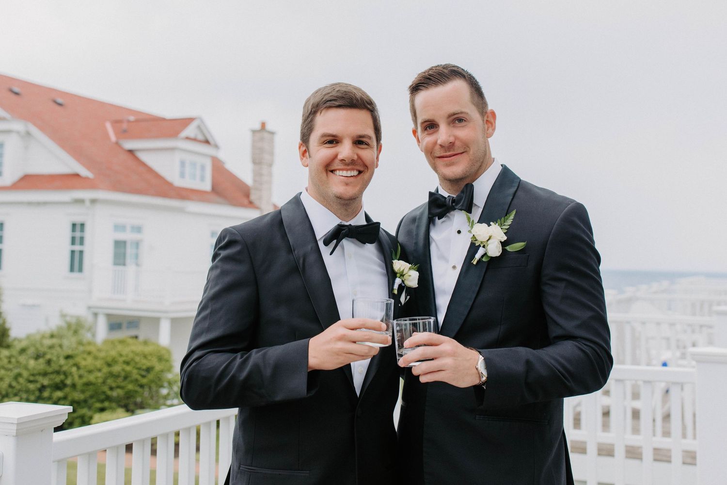 Wedding party toasts with drinks on an oceanfront porch.