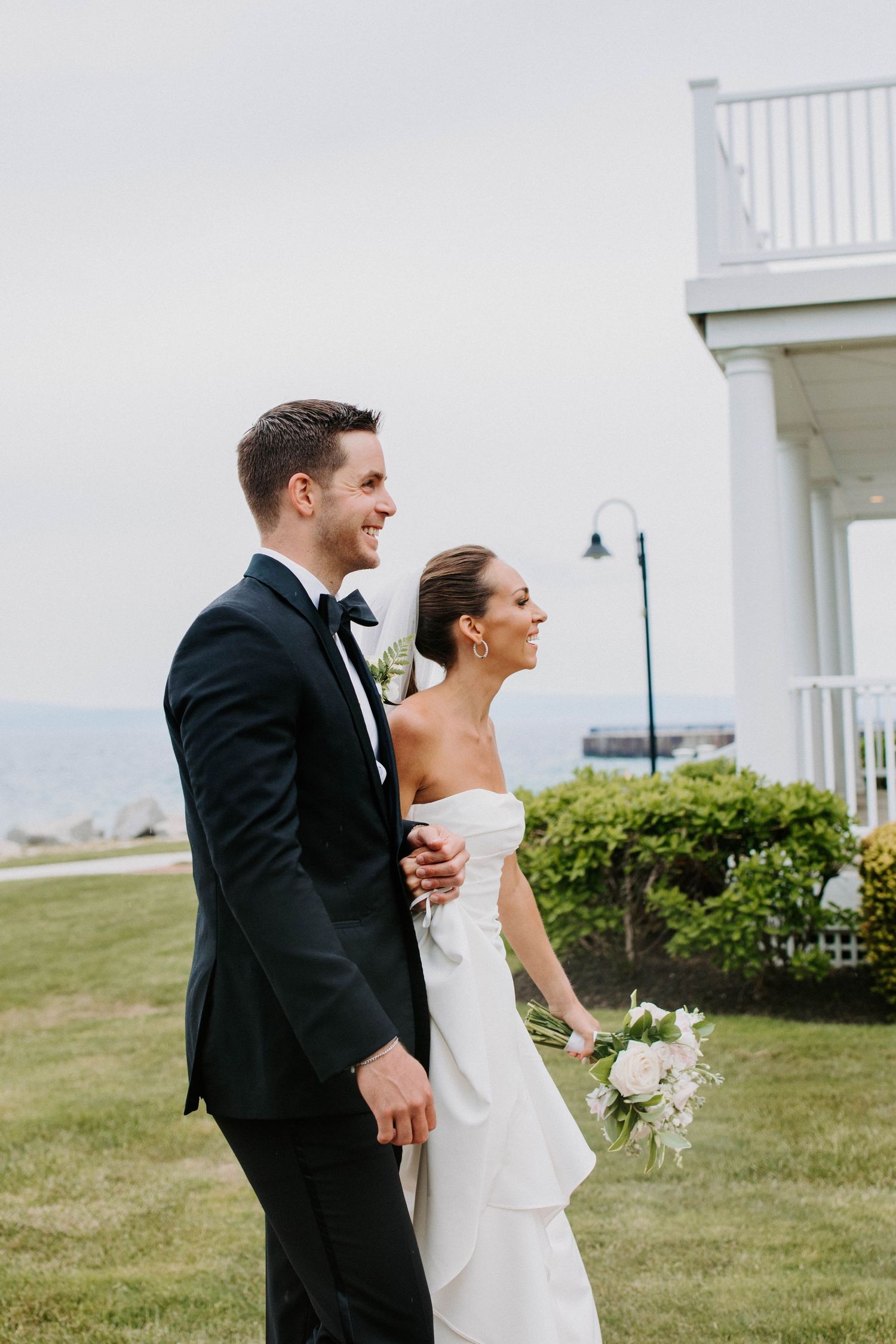 Joyful wedding couple sharing candid moment on manicured lawn by seaside.