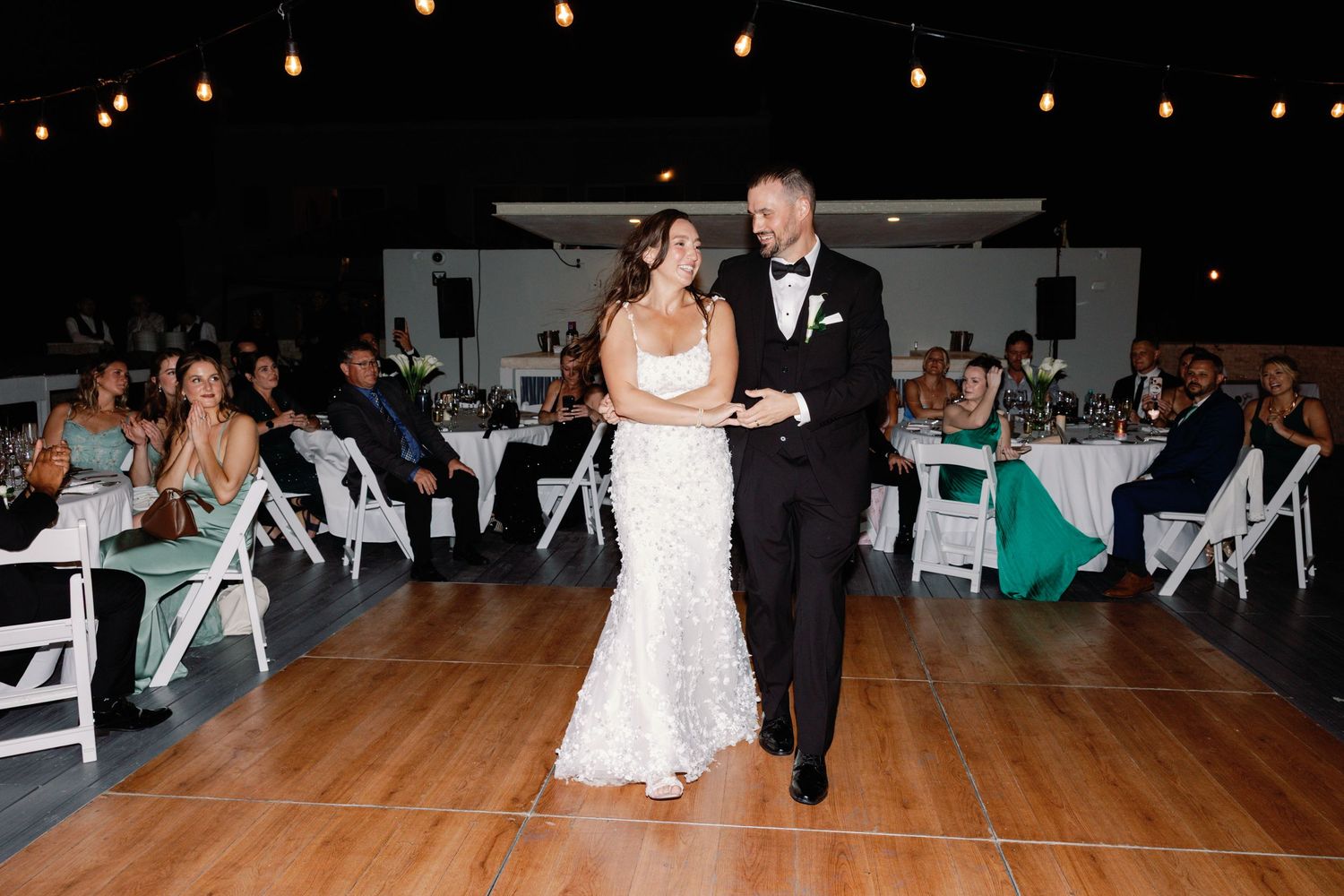 Wedding guests dance and celebrate on a reception dance floor under string lights.