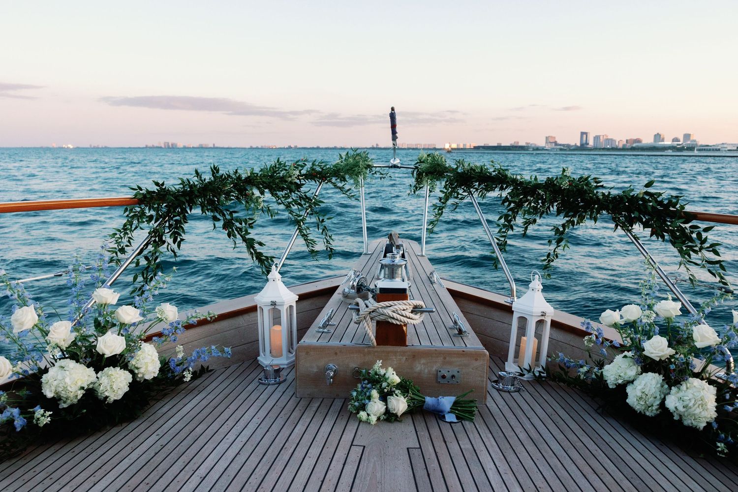 Elegant boat wedding setup with white floral arrangements and lanterns against ocean backdrop.