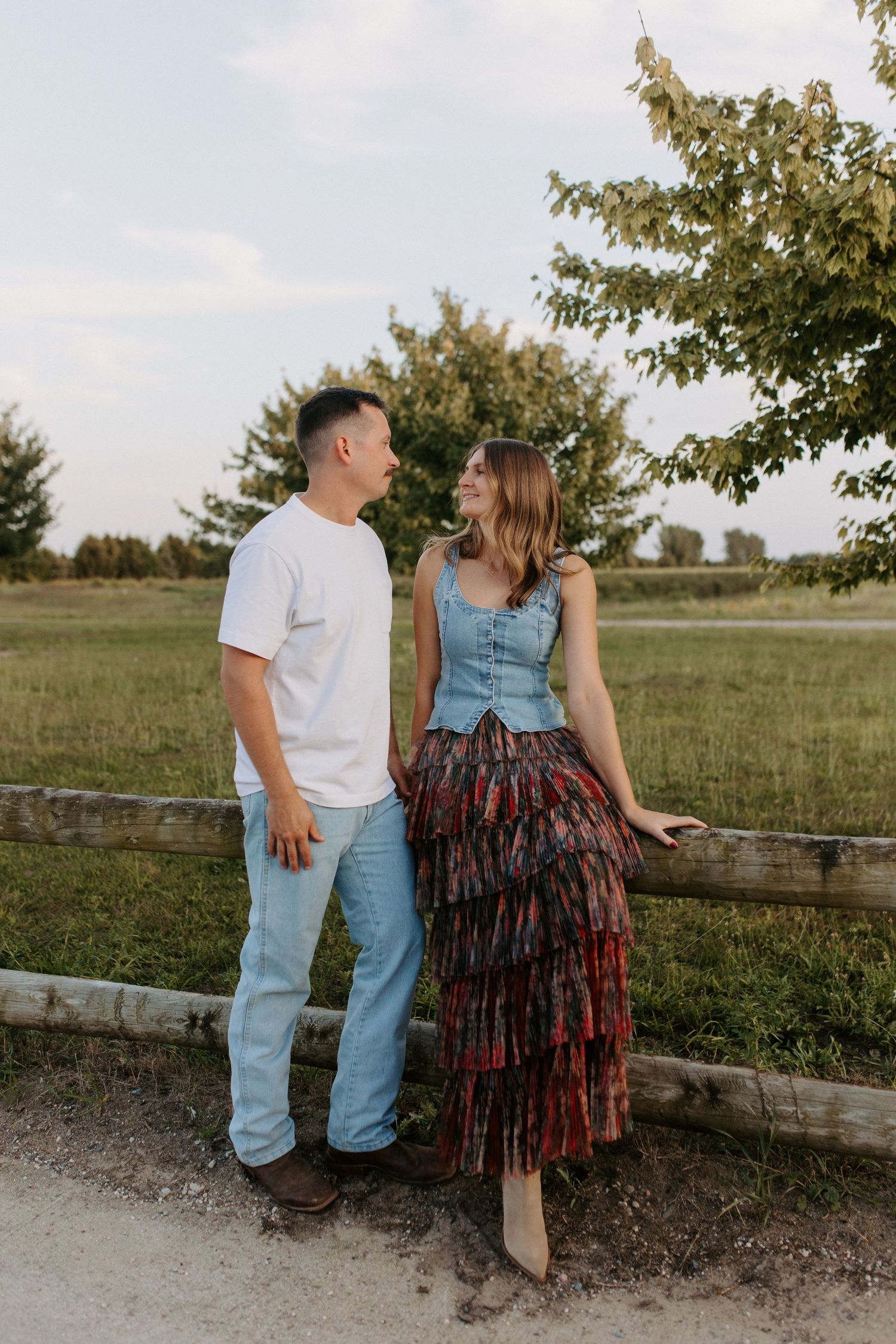 Couple standing by wooden fence in countryside setting.