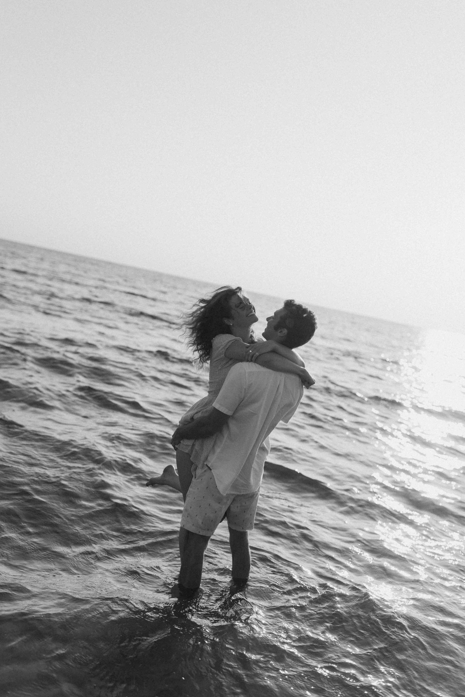 Black and white photo of couple playing in ocean waves.