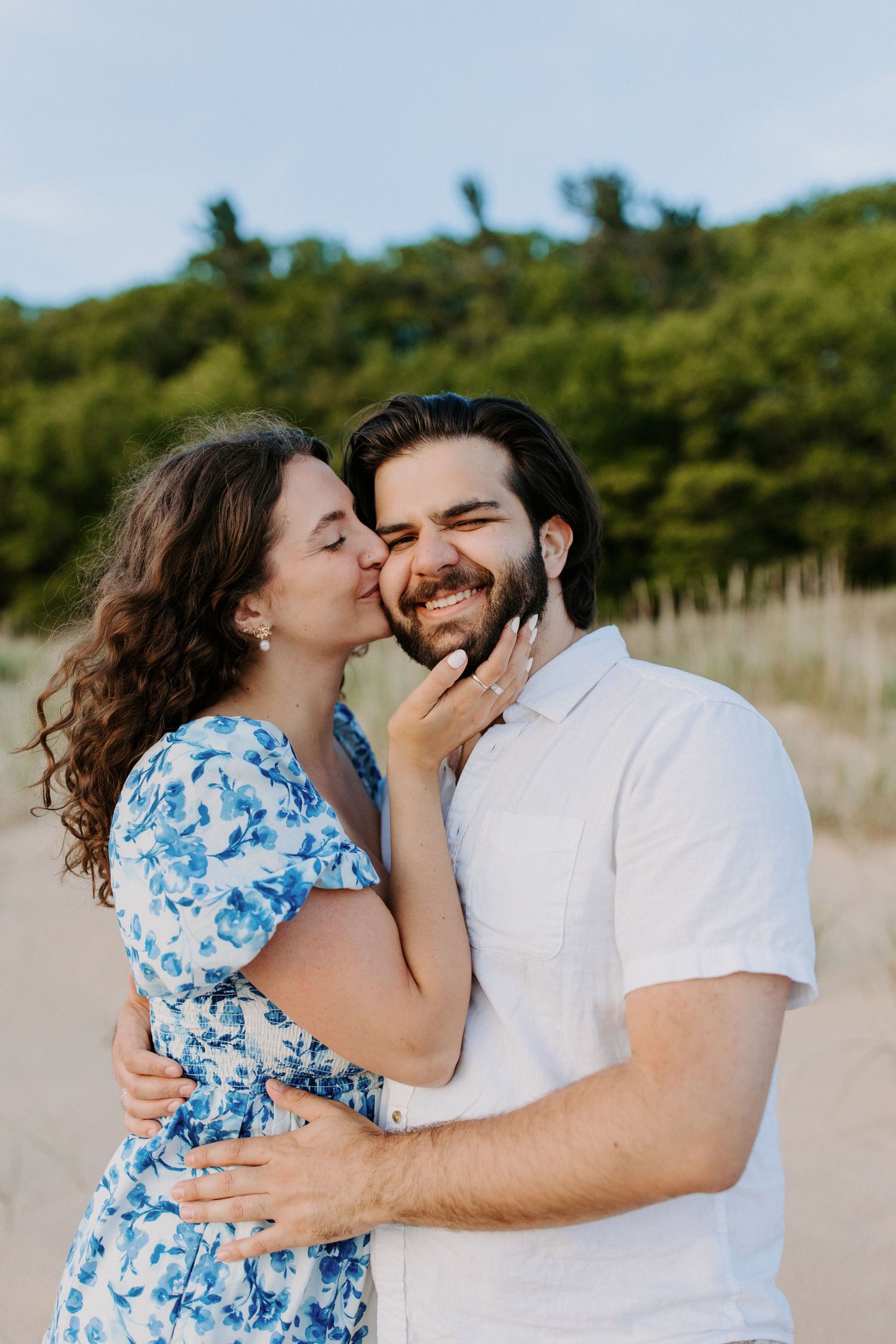Romantic beach photoshoot with couple in blue floral dress and white shirt.