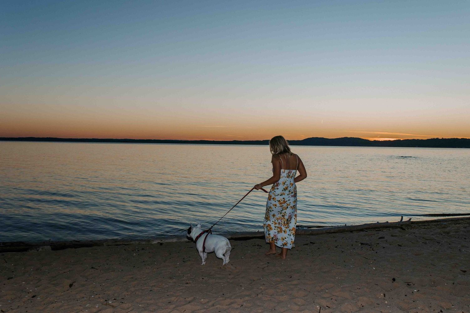 Serene beach landscape at sunset with gentle waves and distant tree-lined shore.