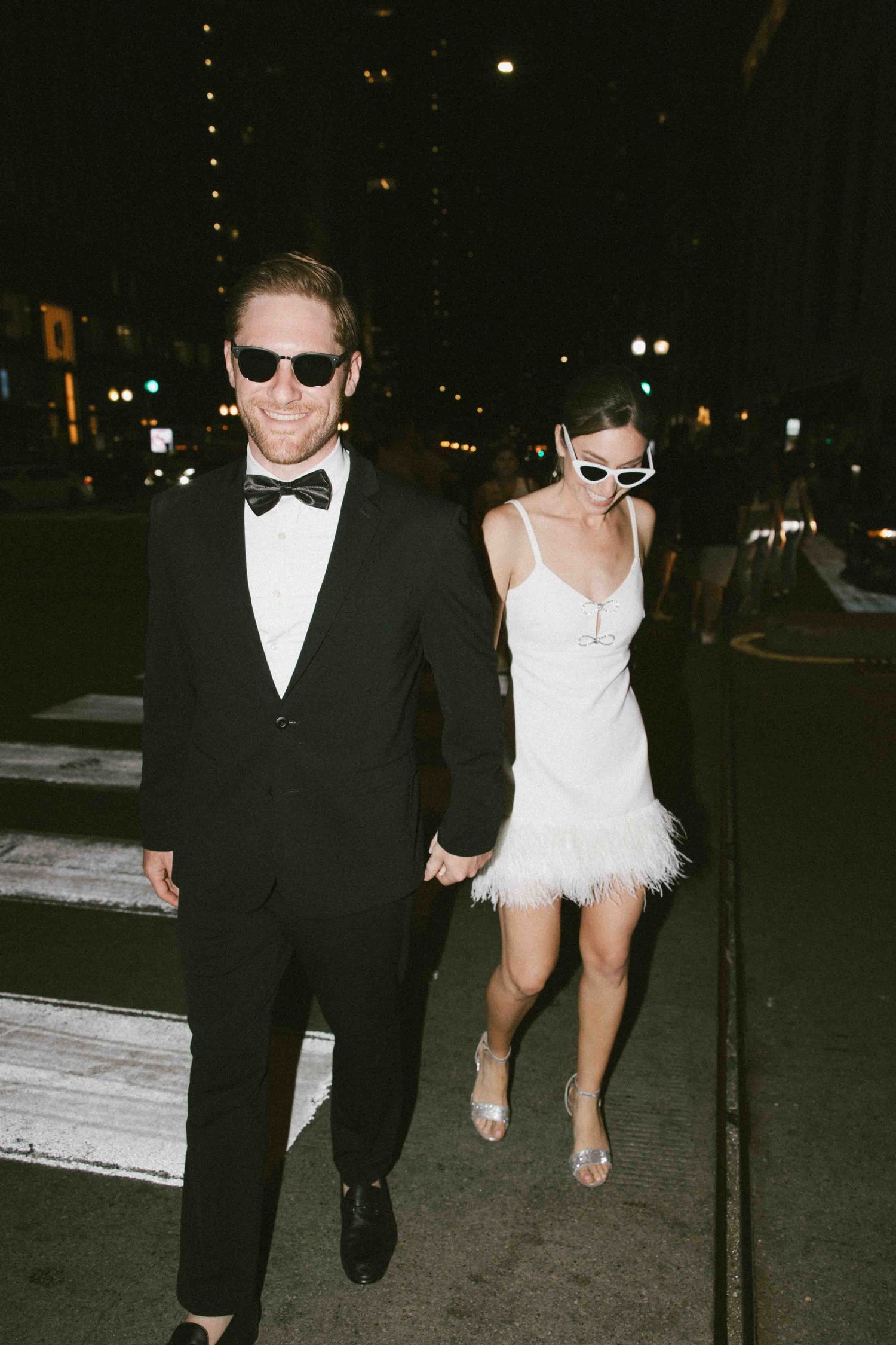 A playful nighttime photo series of a couple in formal wear walking along an urban pathway.