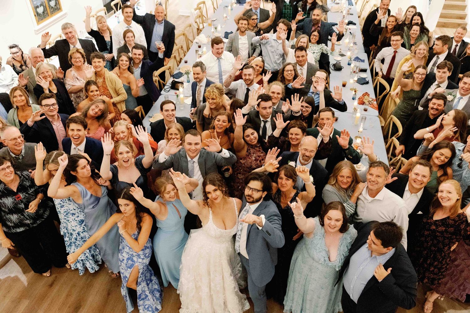 Joyful wedding guests raise their hands in celebration during reception festivities.
