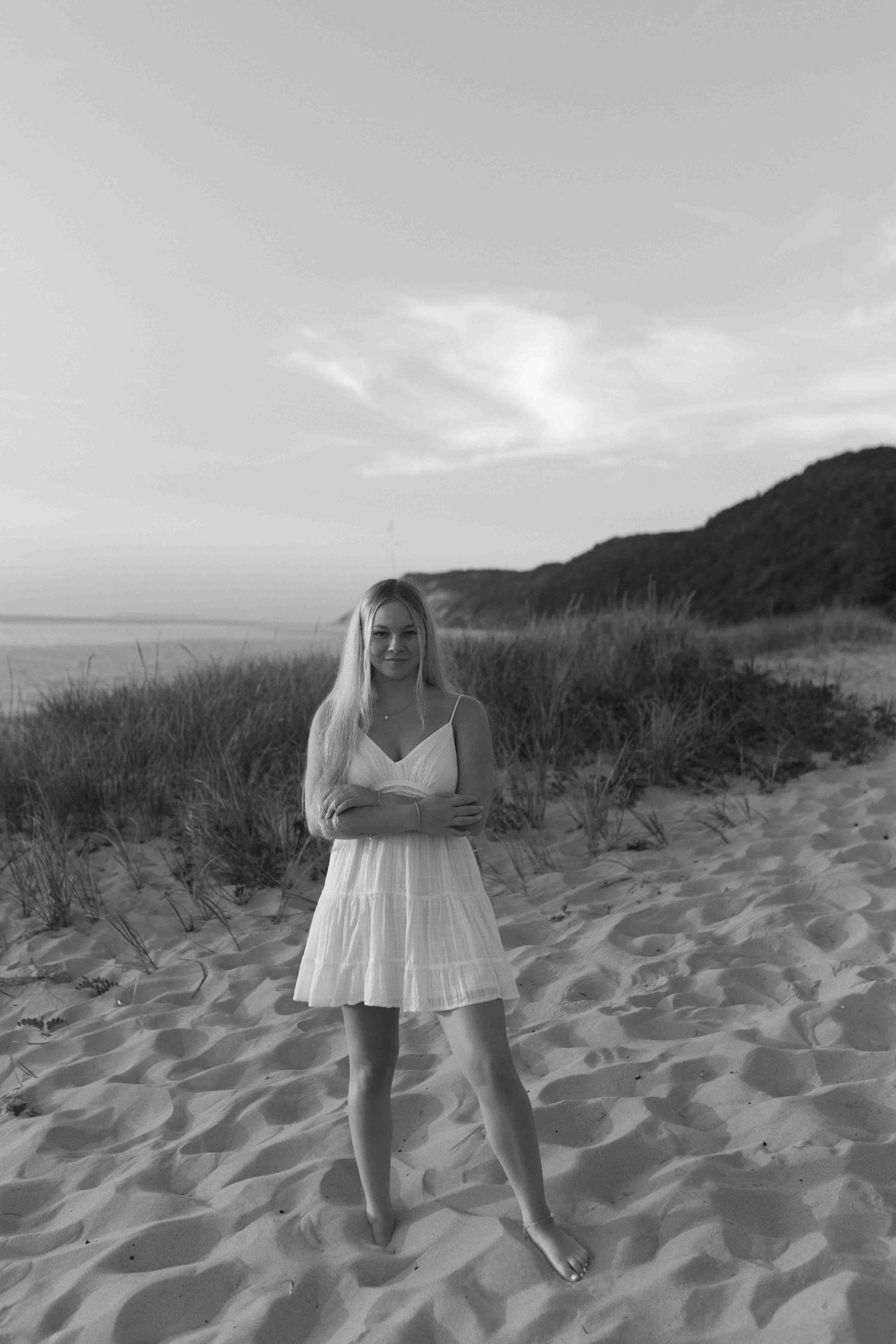 Person in white dress standing on sandy beach dunes in black and white.
