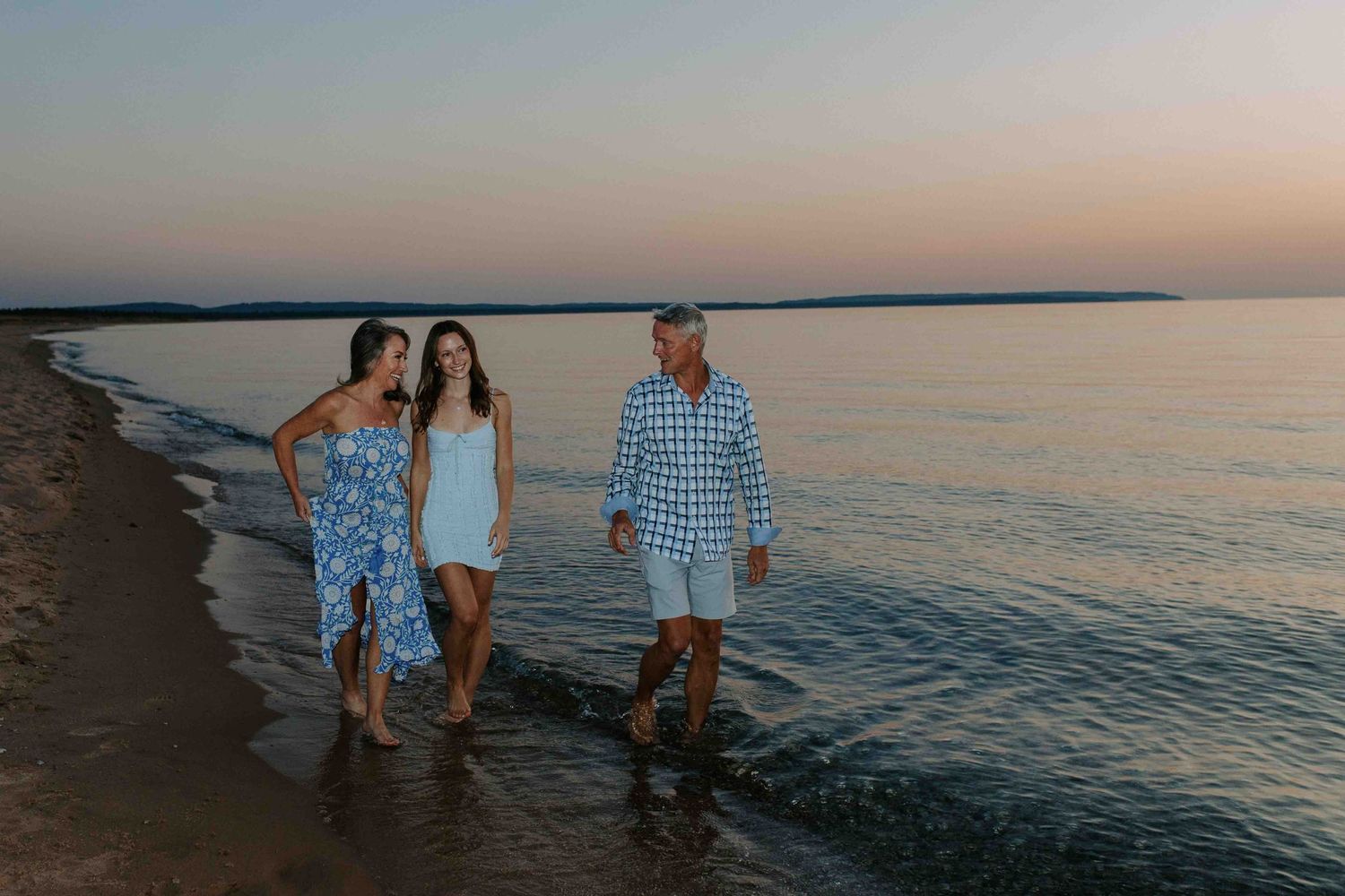 Group walking together along a serene beach shoreline during sunset.