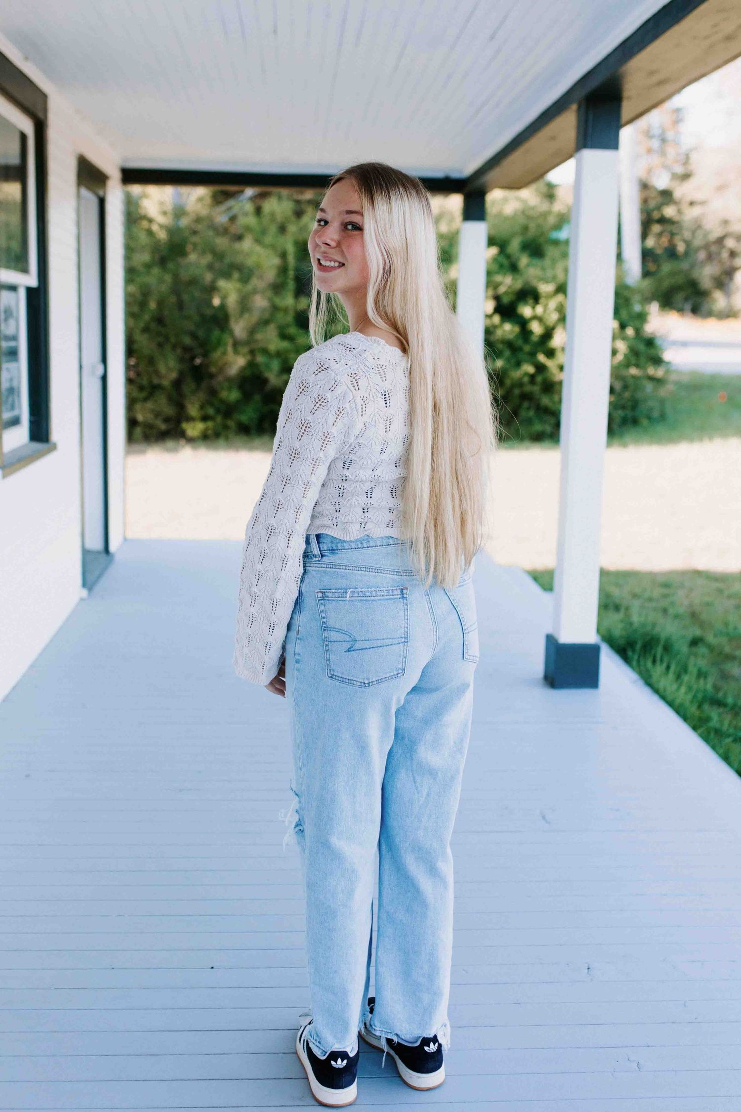 Multiple poses on a white wooden porch wearing a cozy white sweater and vintage-style jeans.