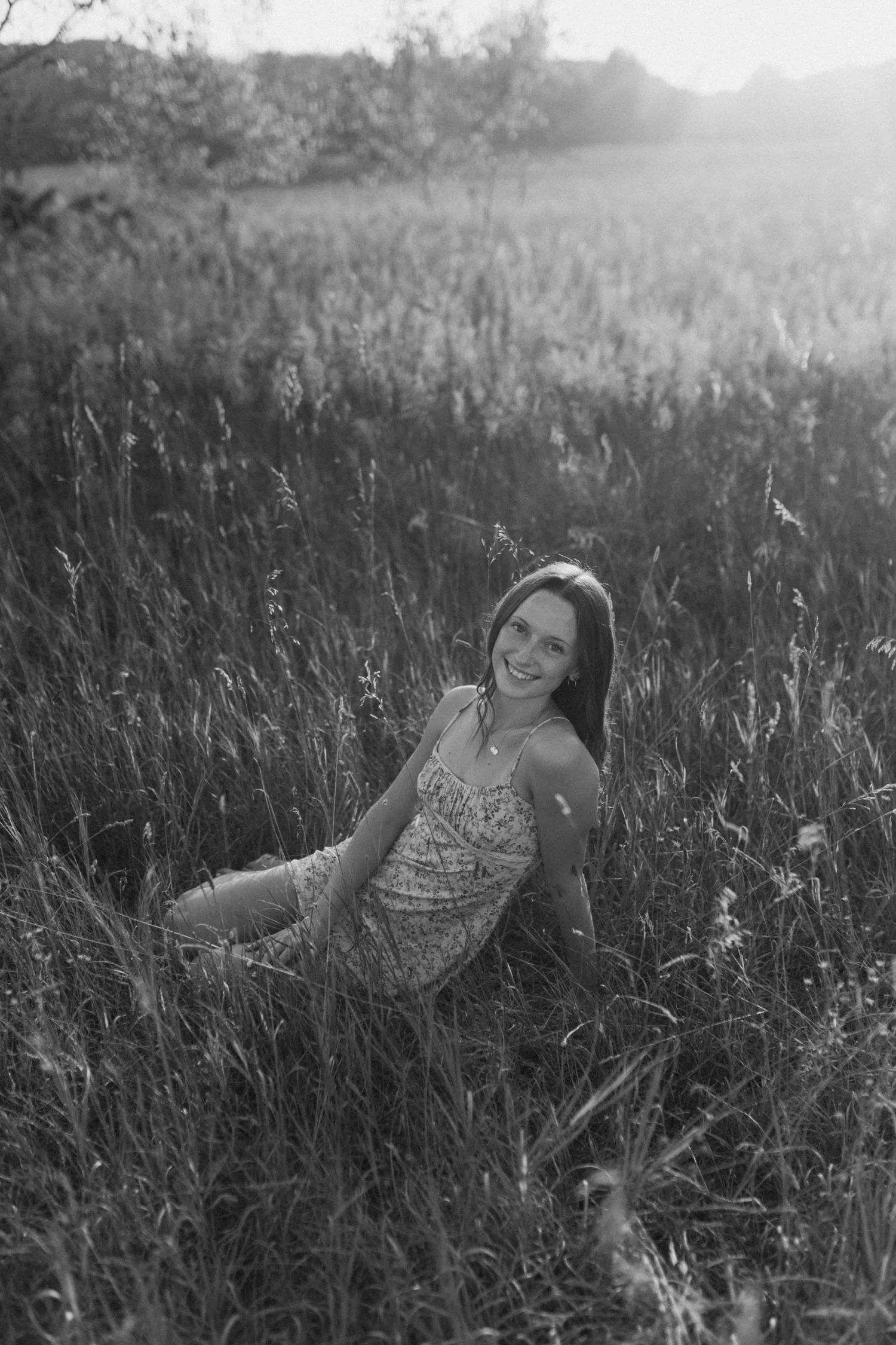 Black and white portrait of someone lying in tall grass during golden hour.