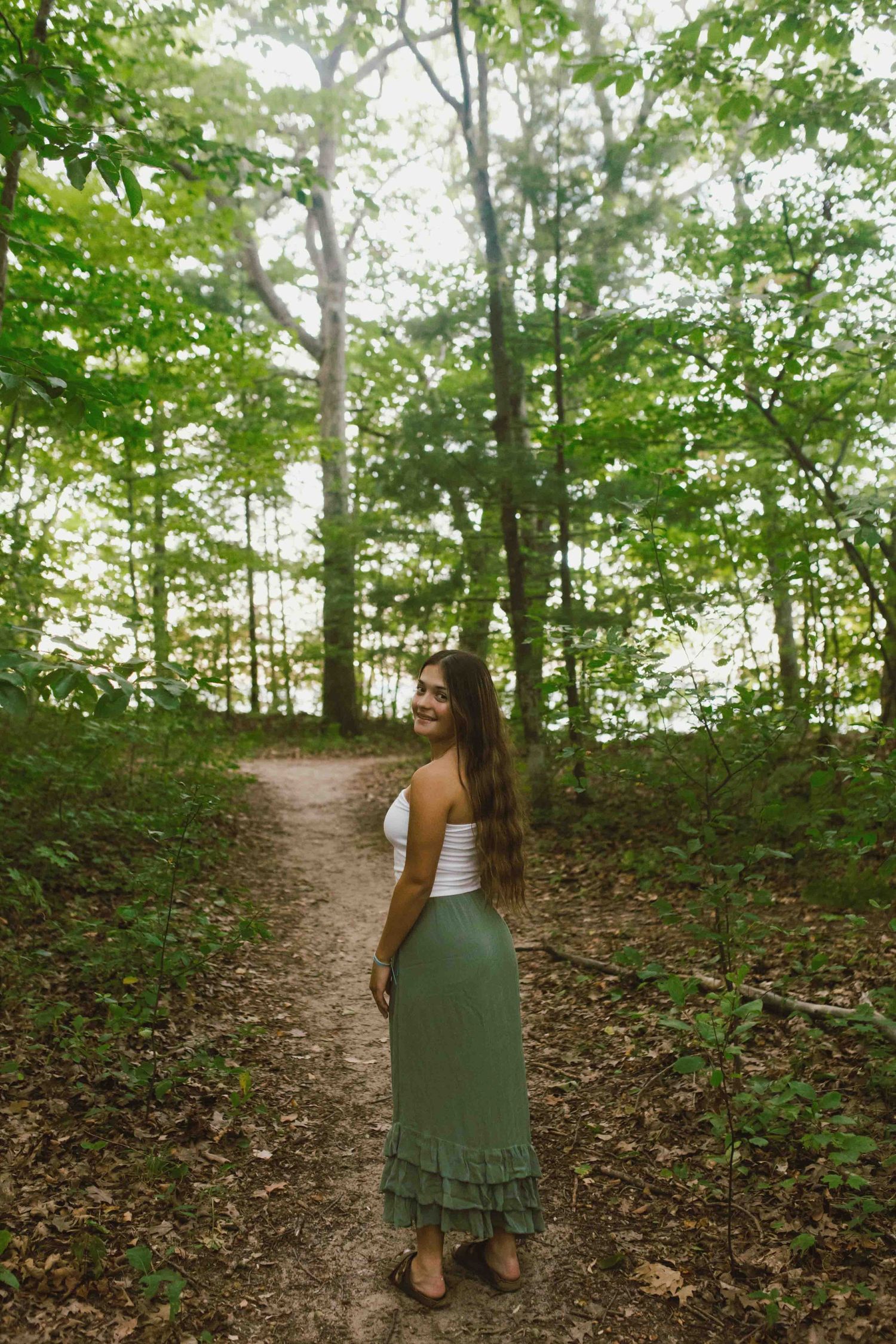A winding dirt path through green summer woods with casual summer fashion in natural lighting.
