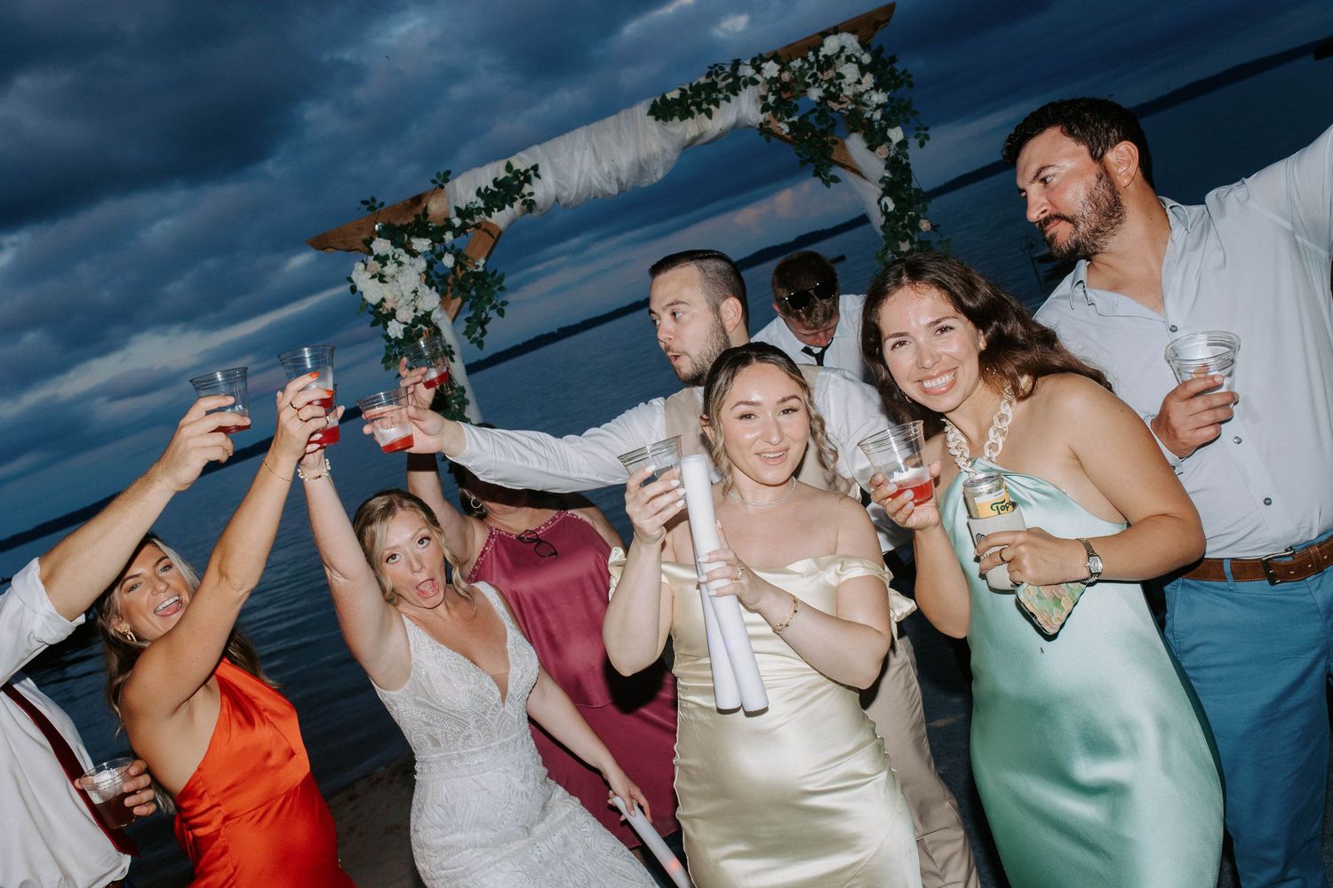 Wedding guests celebrate with drinks and dancing against a dramatic coastal backdrop.