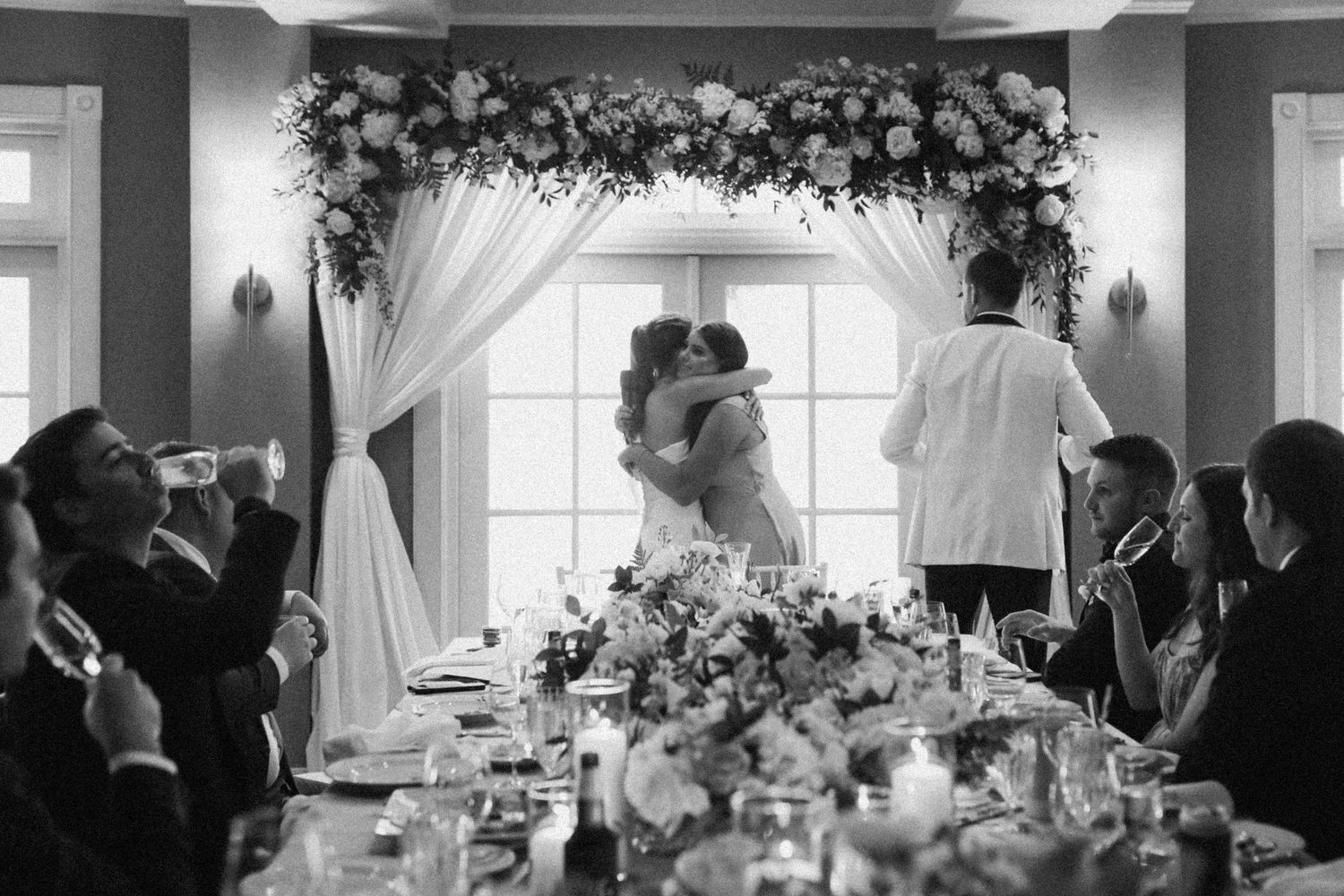 Wedding celebration moment captured under a floral arch with guests applauding at decorated tables.