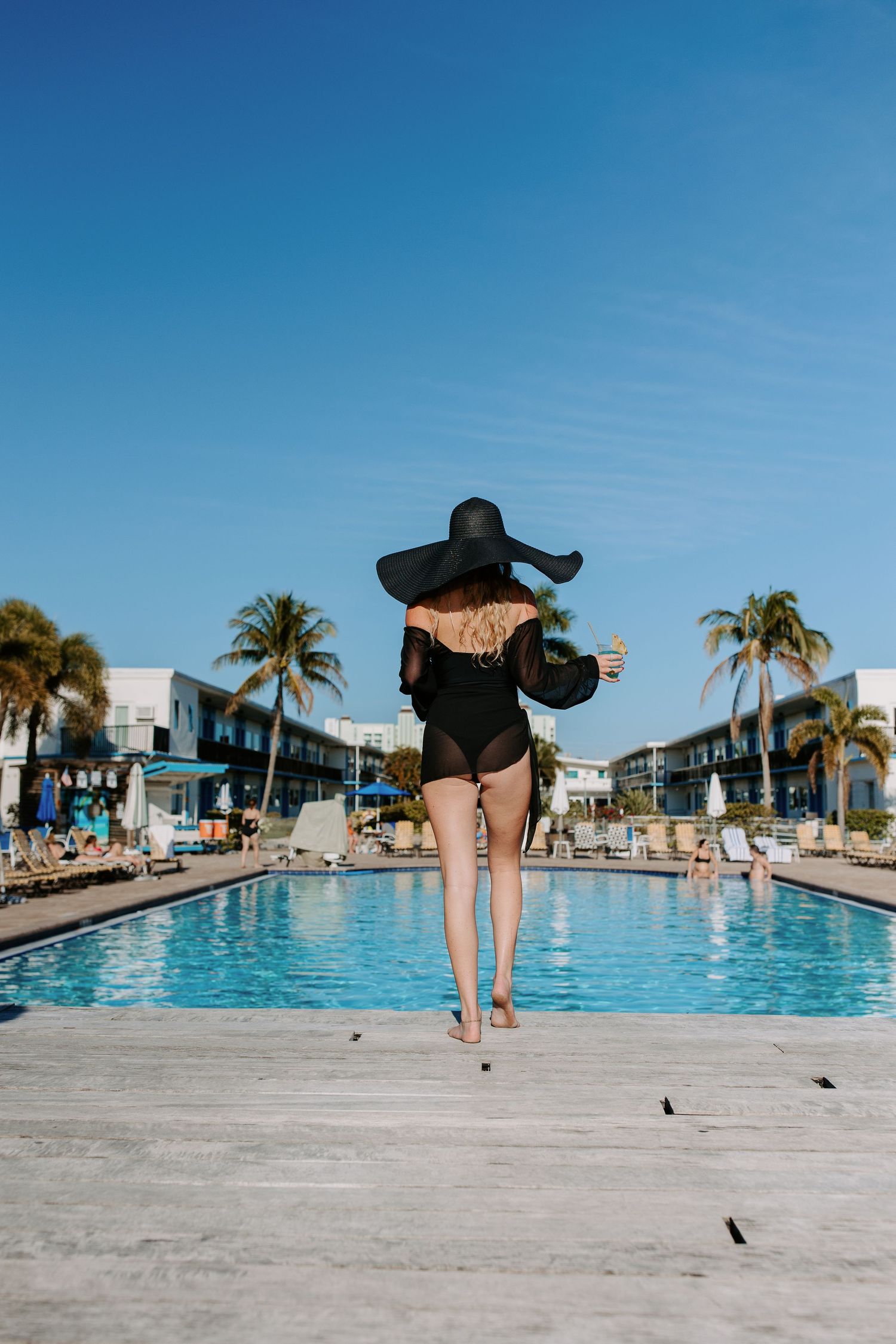 Sequence of photos showing someone jumping into a resort swimming pool on a sunny day with palm trees.