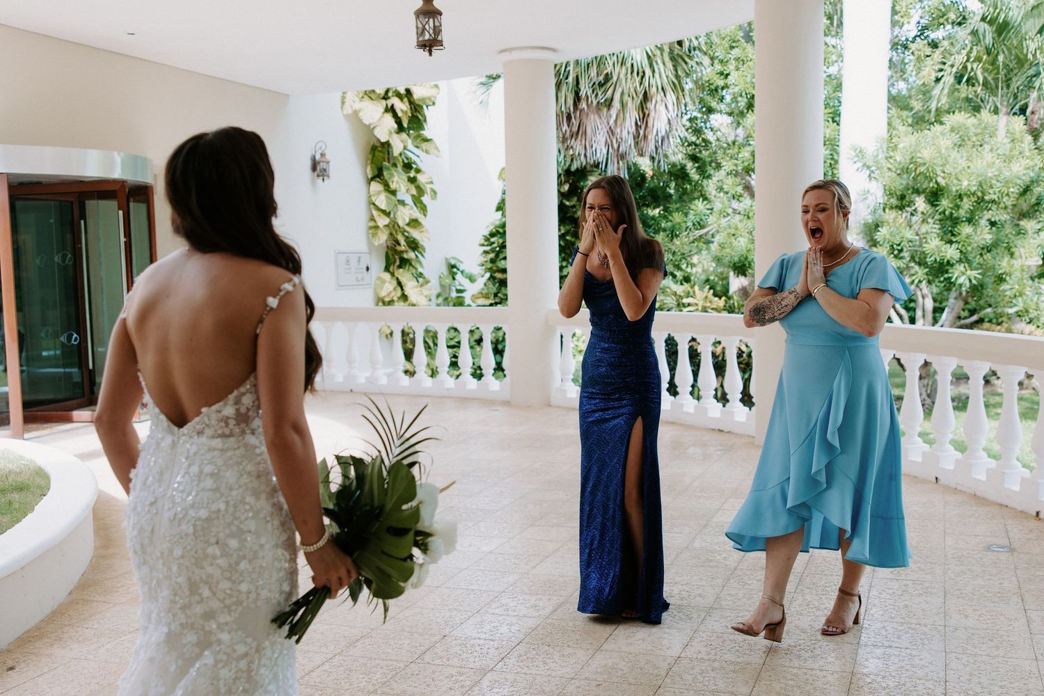 Wedding party members in blue and white dresses walking along elegant columned porch.